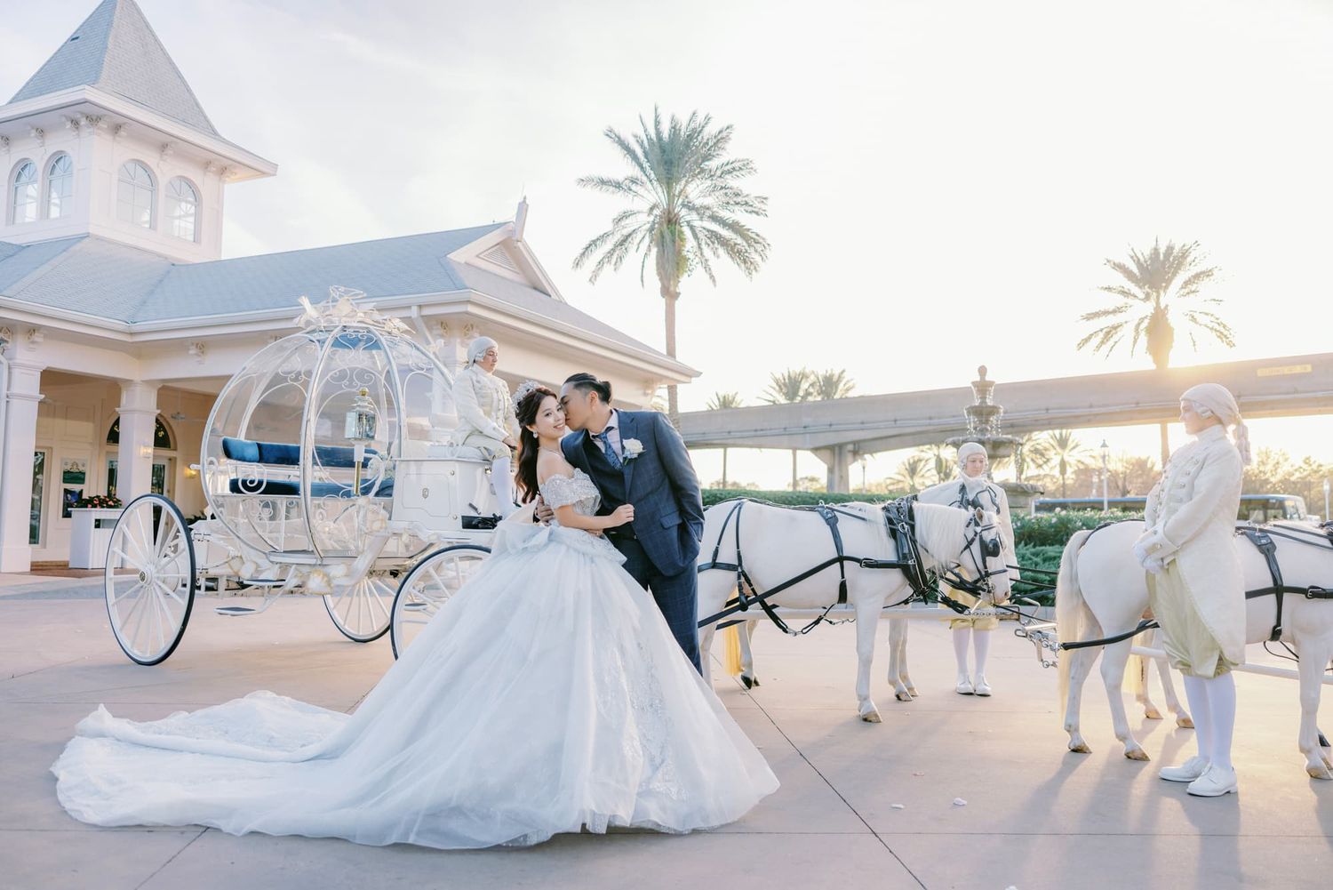 Bride and groom kissing beside a white Cinderella horse-drawn carriage at a Disney wedding venue.