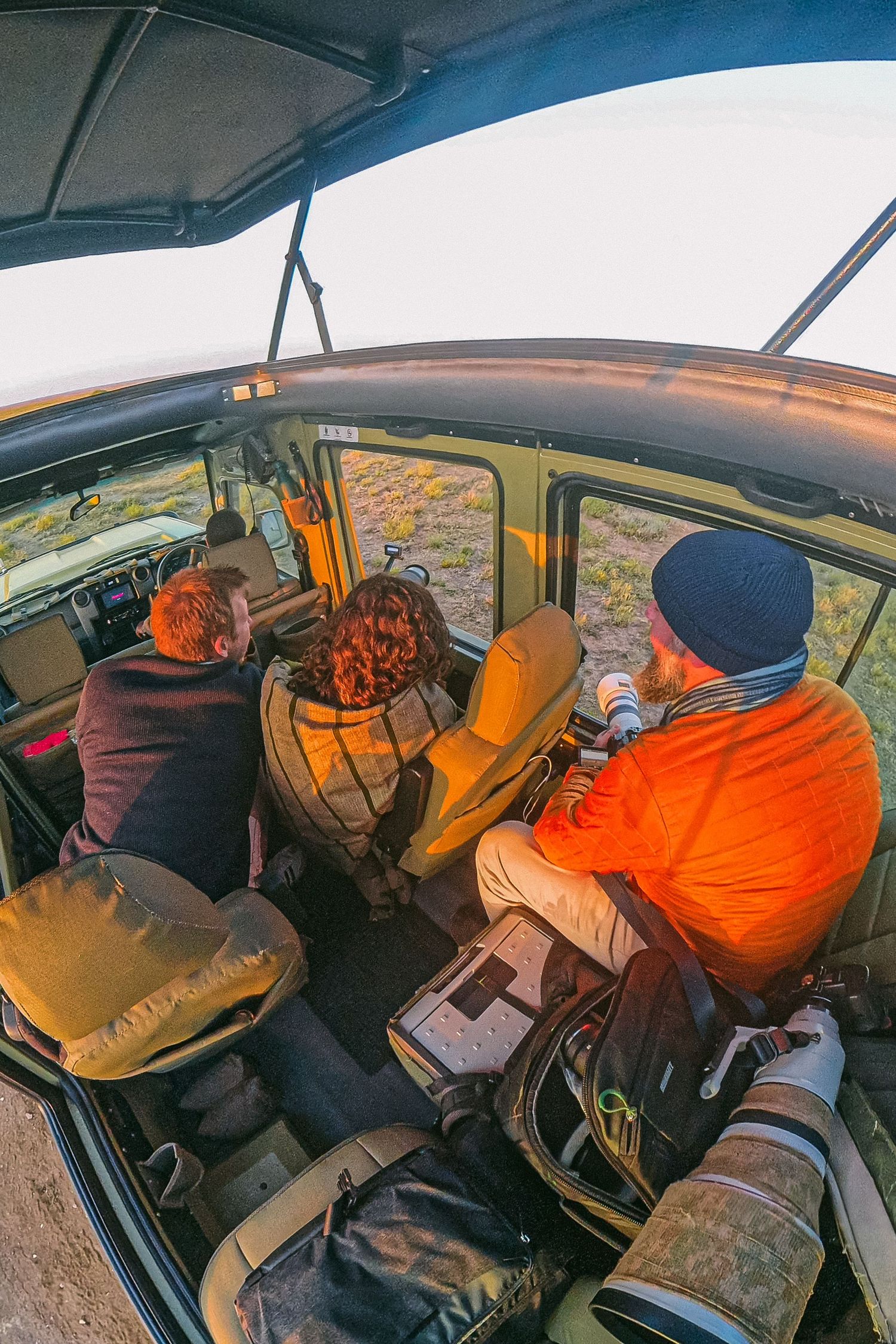 Interior view of safari vehicle with tourists on game drive, photographed with fisheye lens at golden hour.