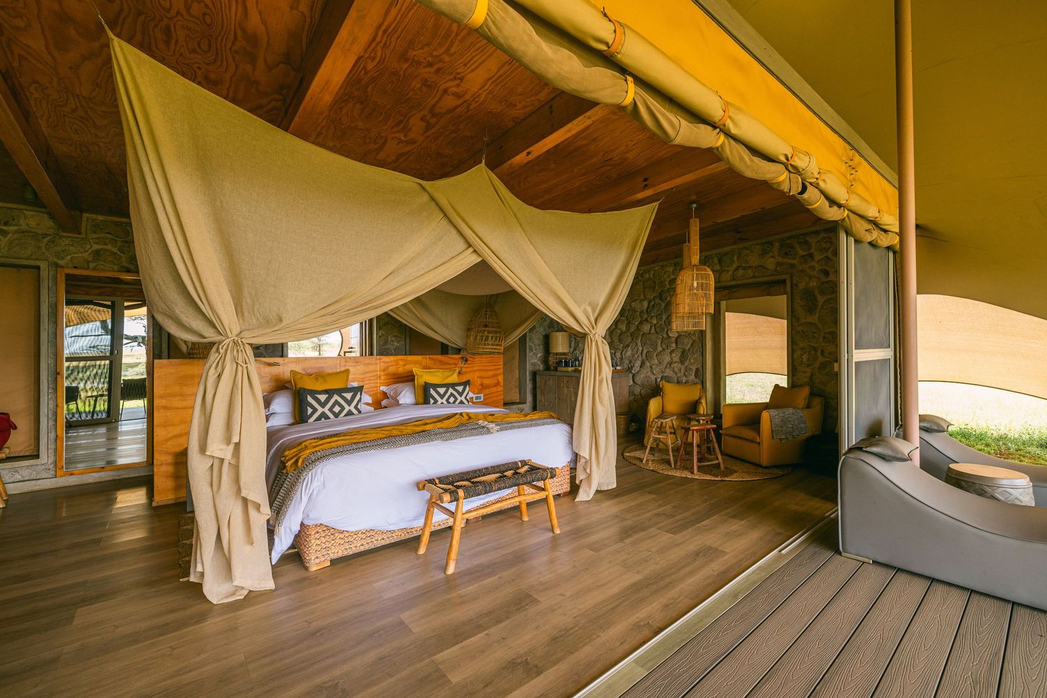 Luxury safari tent bedroom with canopy bed, wooden deck, and elegant neutral decor in a glamping resort.