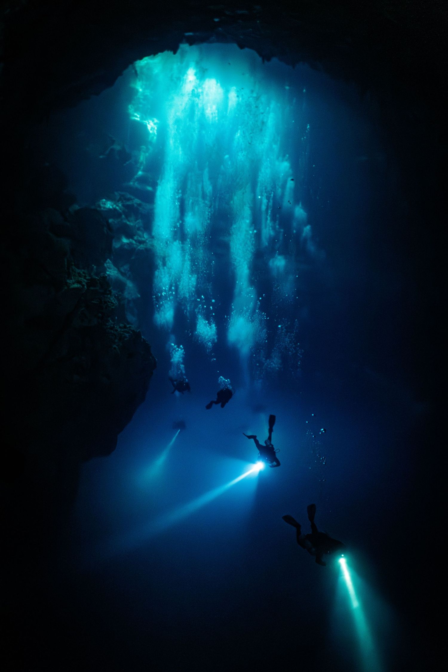 Scuba divers explore an underwater cave illuminated by bright blue lights creating an ethereal underwater atmosphere.
