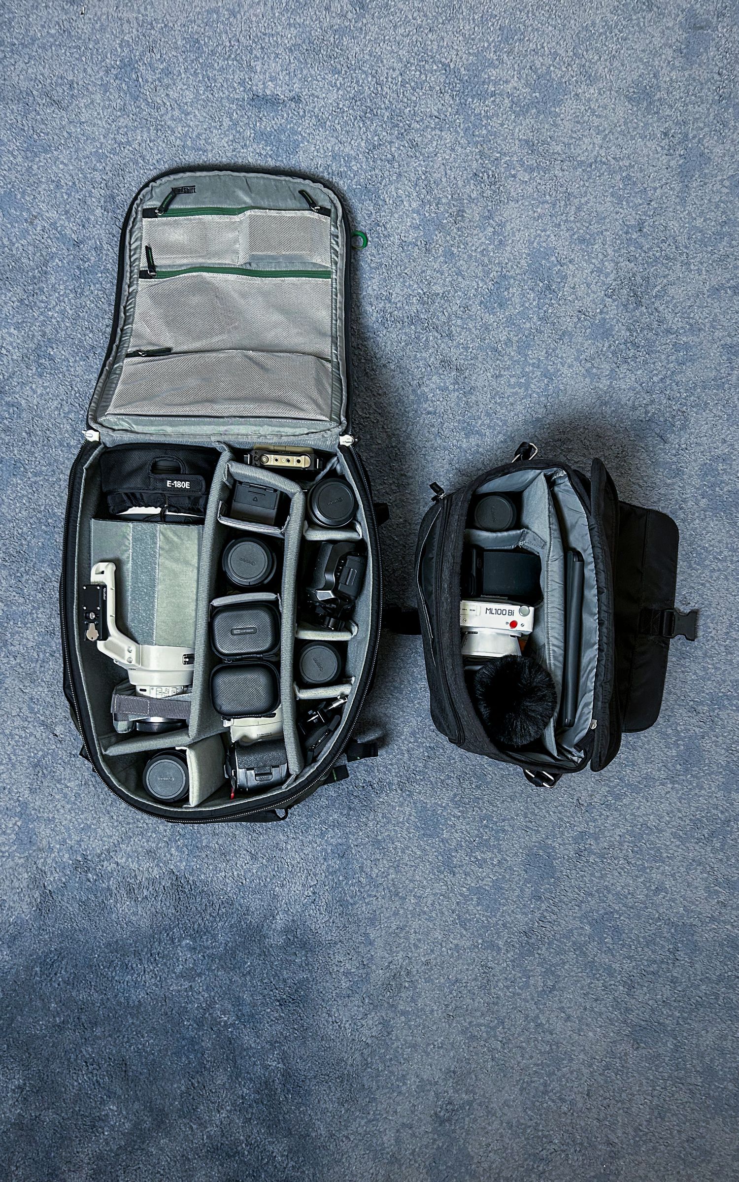 Camera bag and equipment shown in various stages of packing on a gray textured surface.