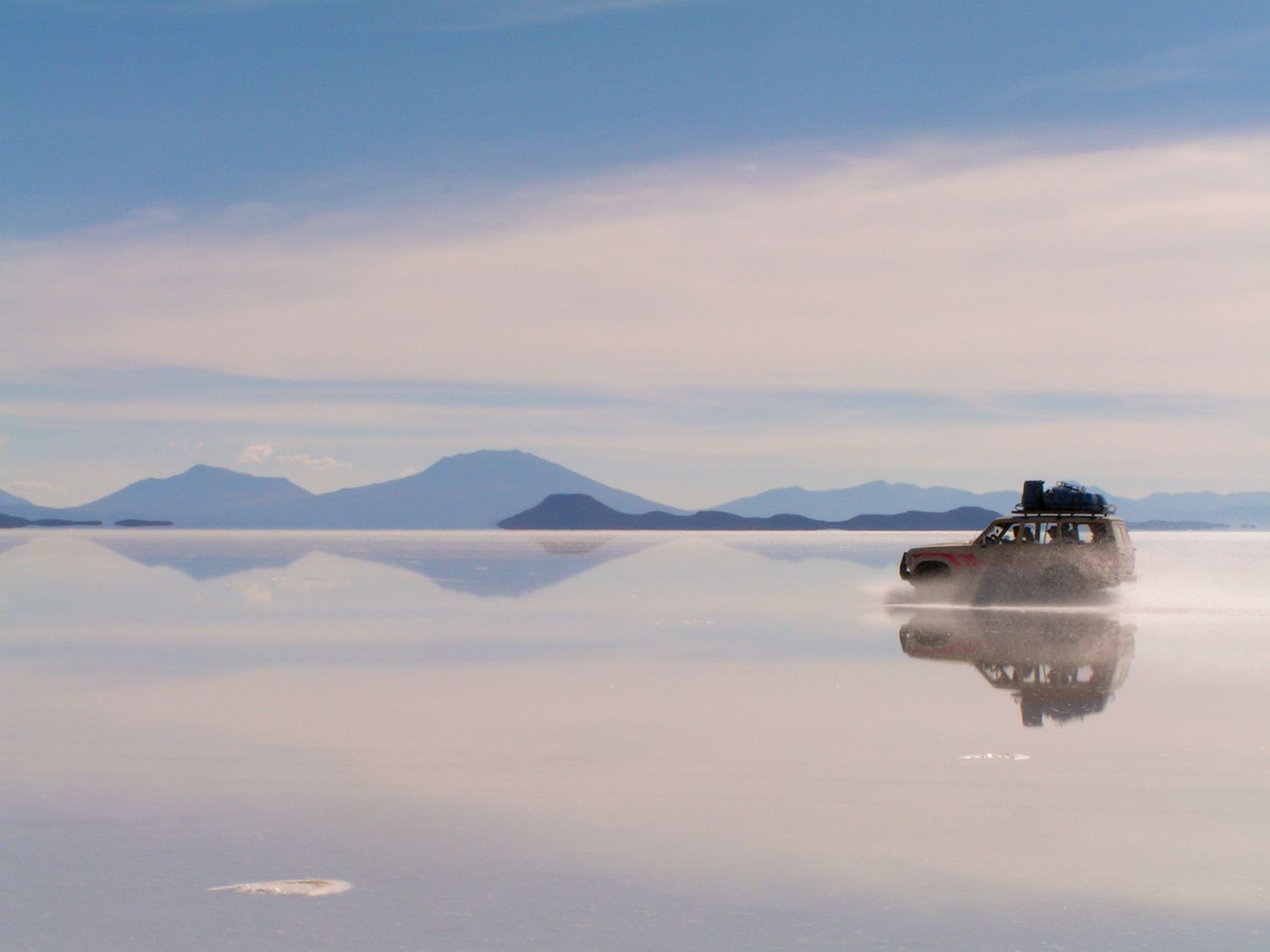A panoramic view of the Salar de Uyuni salt flats in Bolivia reflecting clouds in its mirror-like surface during sunset.