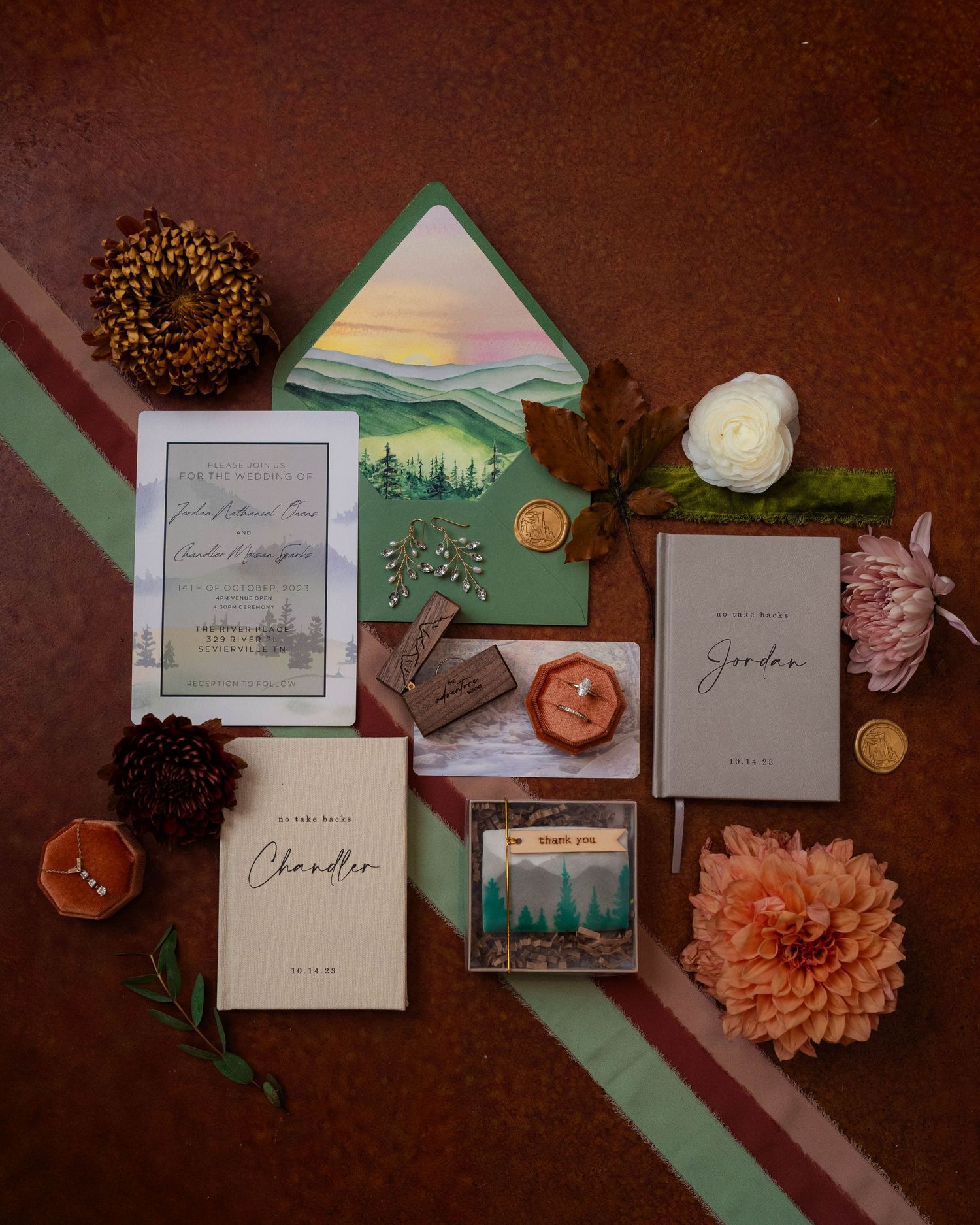 Wedding invitation suite with mountain artwork, florals, and stationery flat lay.