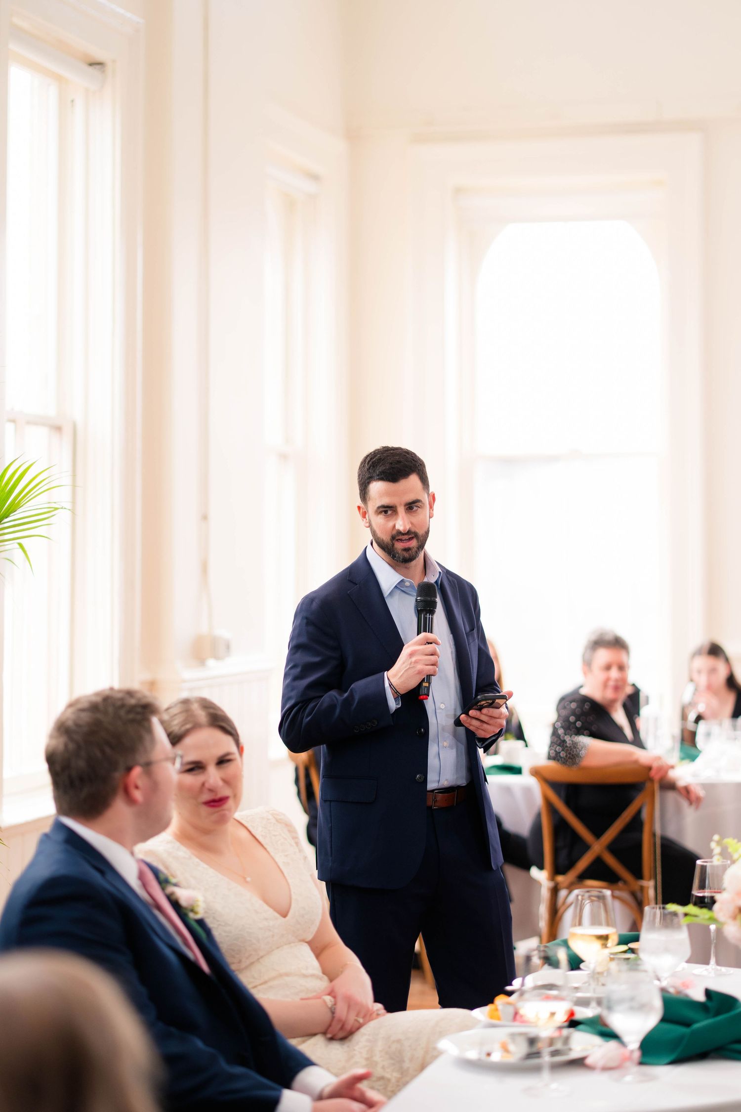 Best man delivers heartfelt speech with microphone to bride and groom at wedding reception.