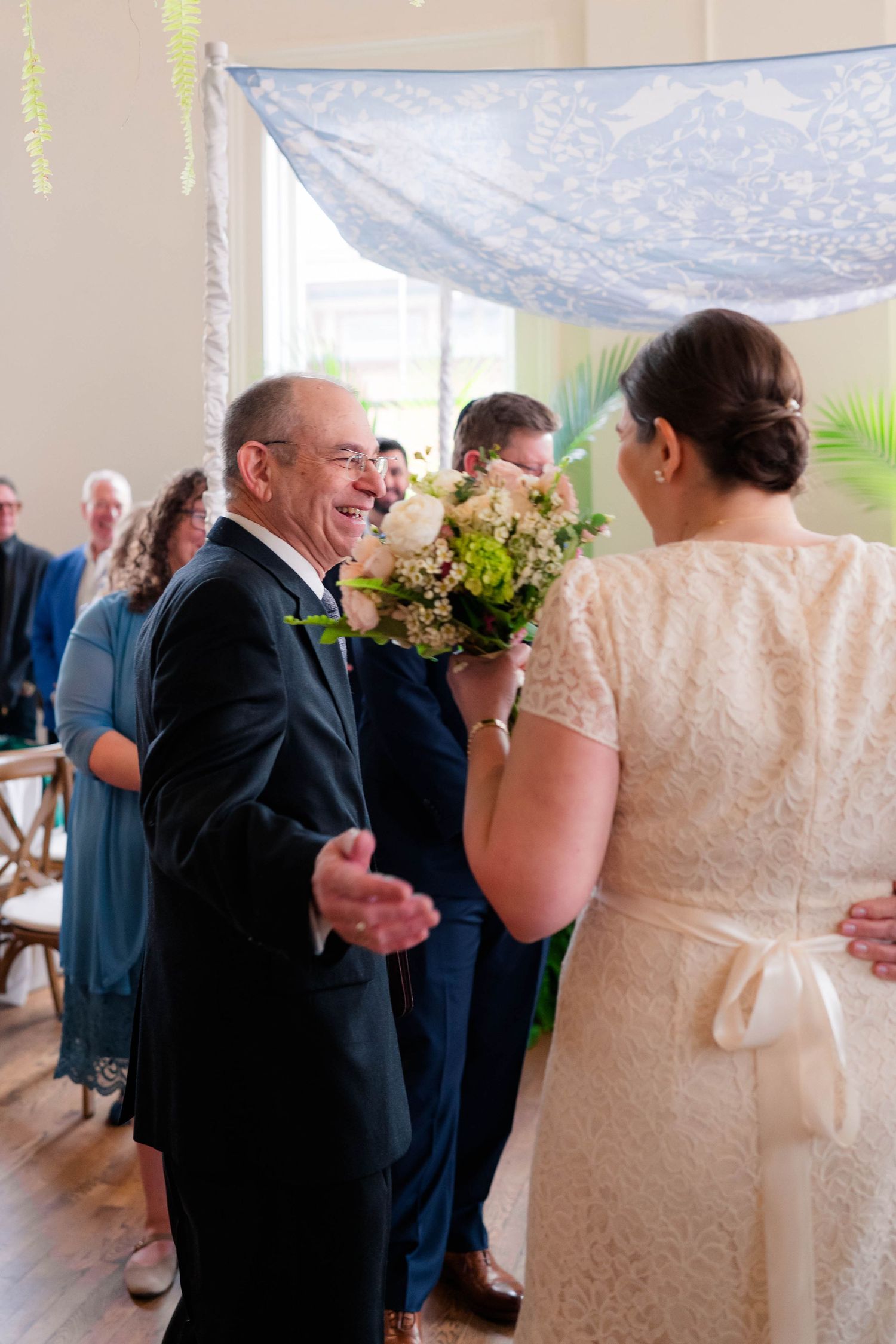 Emotional father reaches for bride in lace gown holding pink bouquet at wedding ceremony altar.