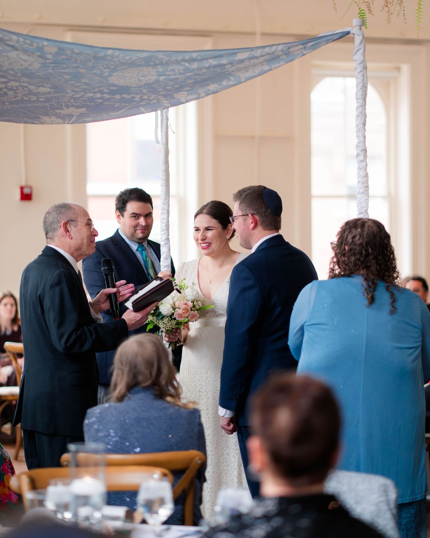 Bride and groom exchange vows under a chuppah during an indoor Jewish wedding ceremony.