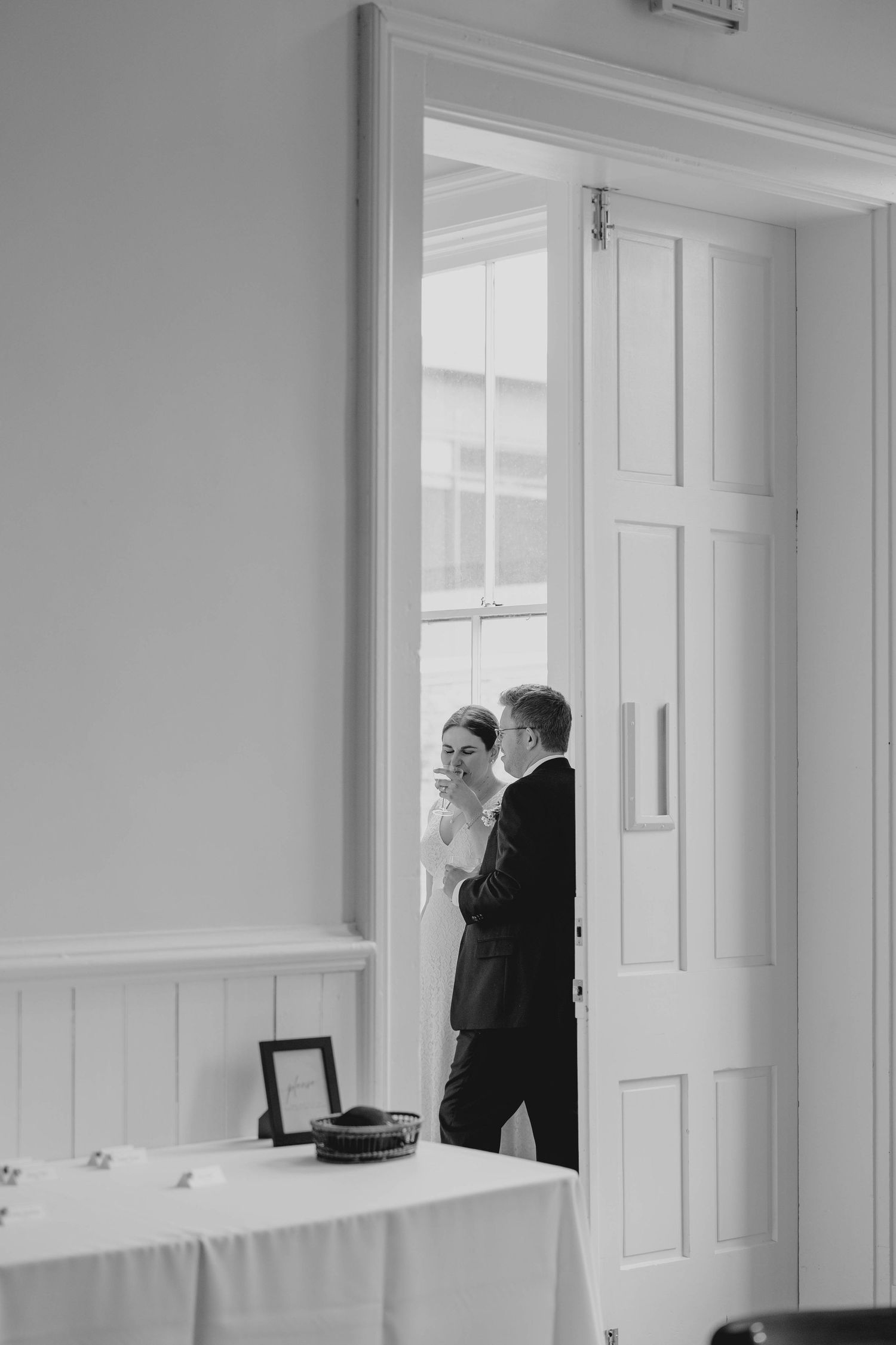 Black and white photo of bride and groom sharing a quiet moment through open white doors.