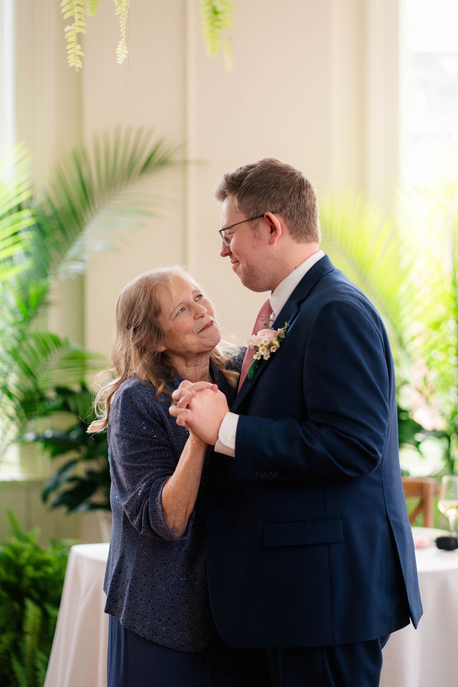 Groom in navy suit dancing with mother in blue dress at wedding reception.
