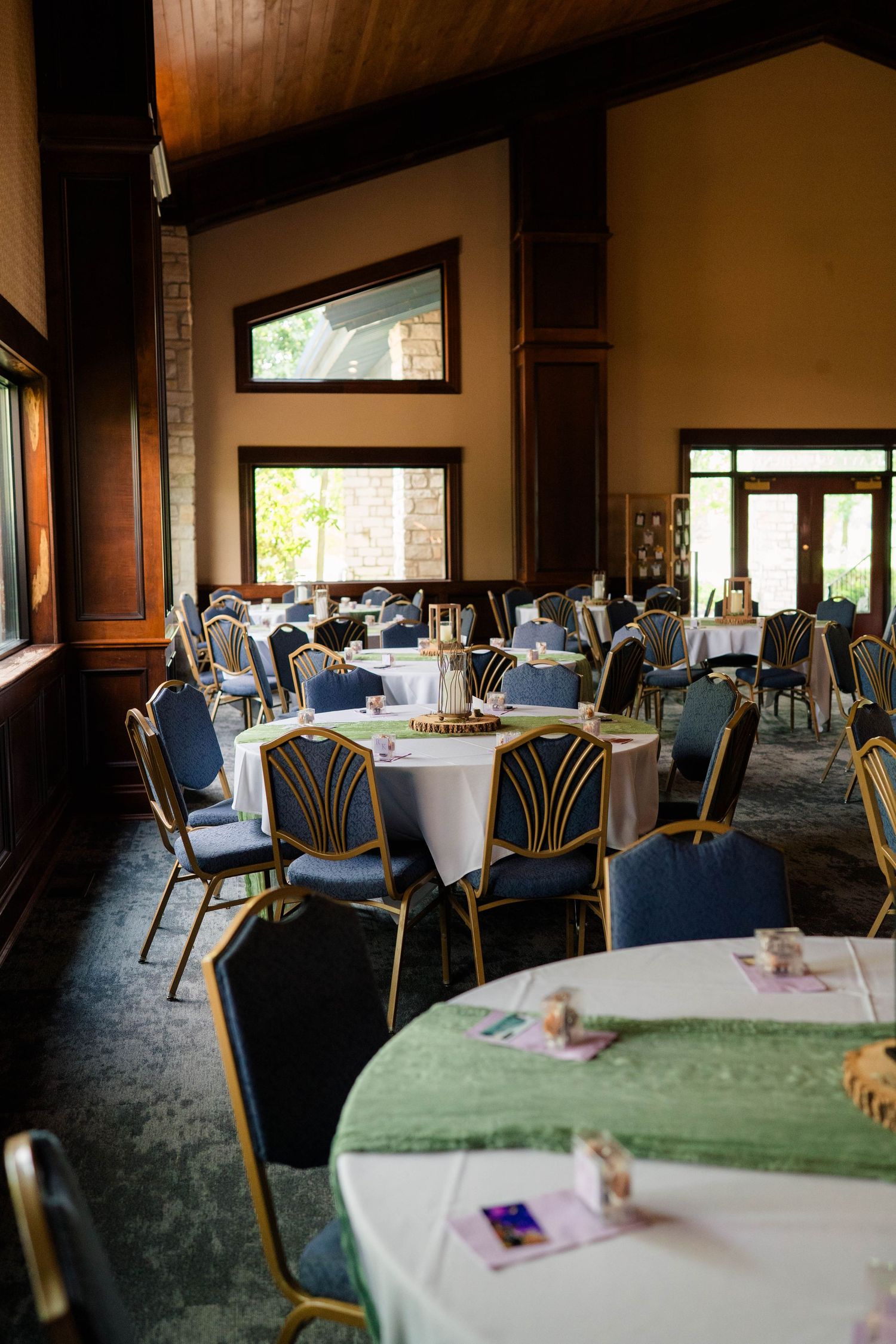 Elegant wedding reception hall with round tables, green runners, blue chairs, and warm lighting.