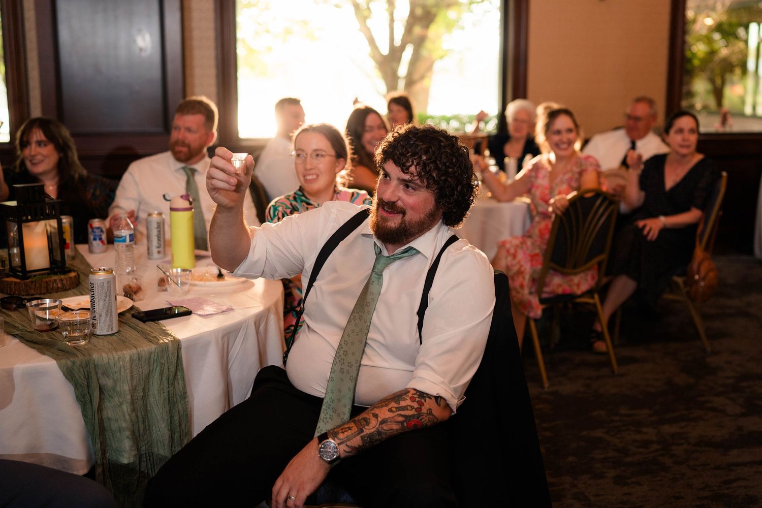 Tattooed wedding guest raising a glass for a toast at the reception.