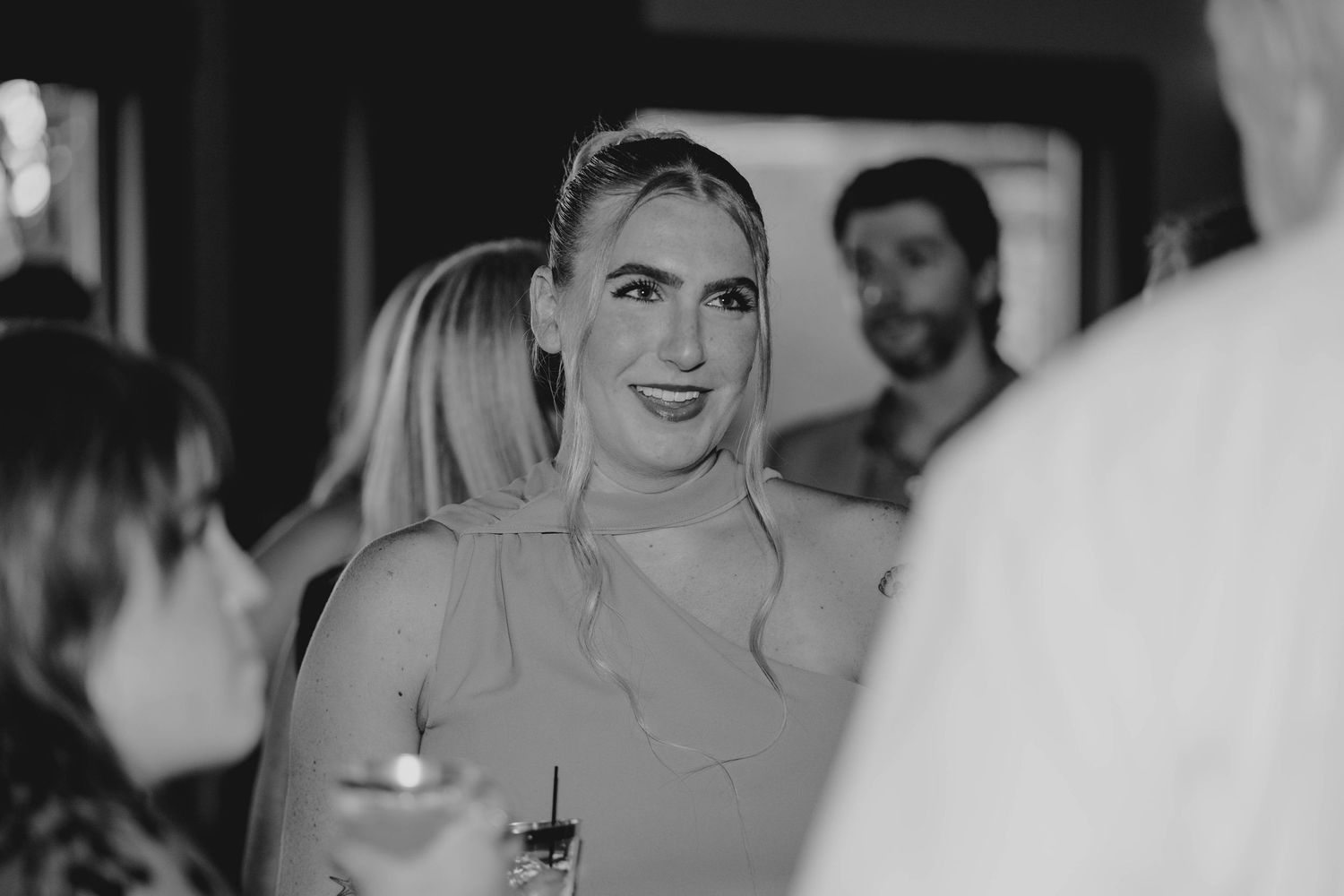 Wedding guest smiles and socializes holding a drink at an indoor wedding reception.