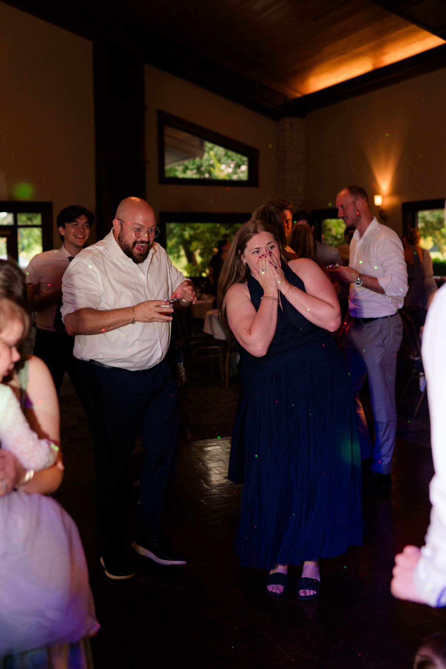 Guests dancing and laughing at an indoor wedding reception with warm ambient lighting.