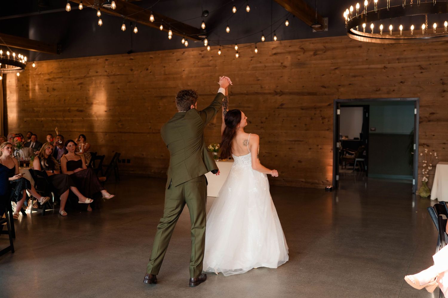 Bride and groom share first dance under string lights in rustic brick industrial wedding venue.