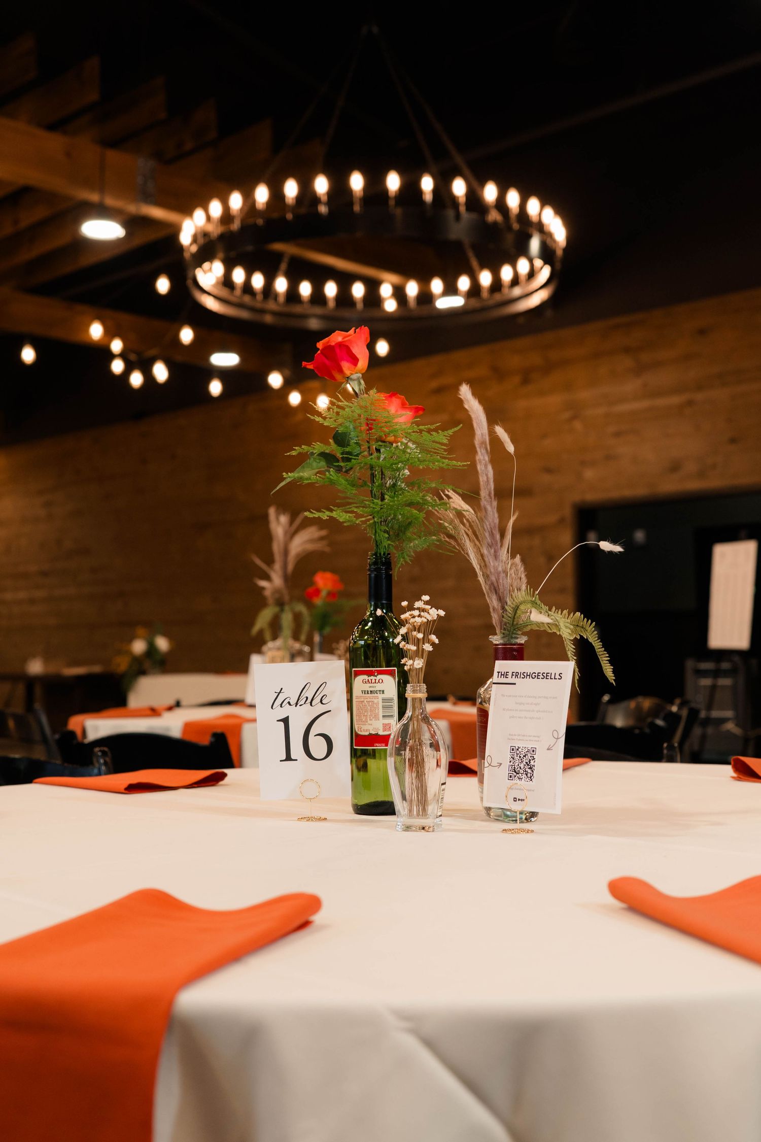 Wedding reception table 16 with orange napkins, wine bottle centerpiece, and red rose.