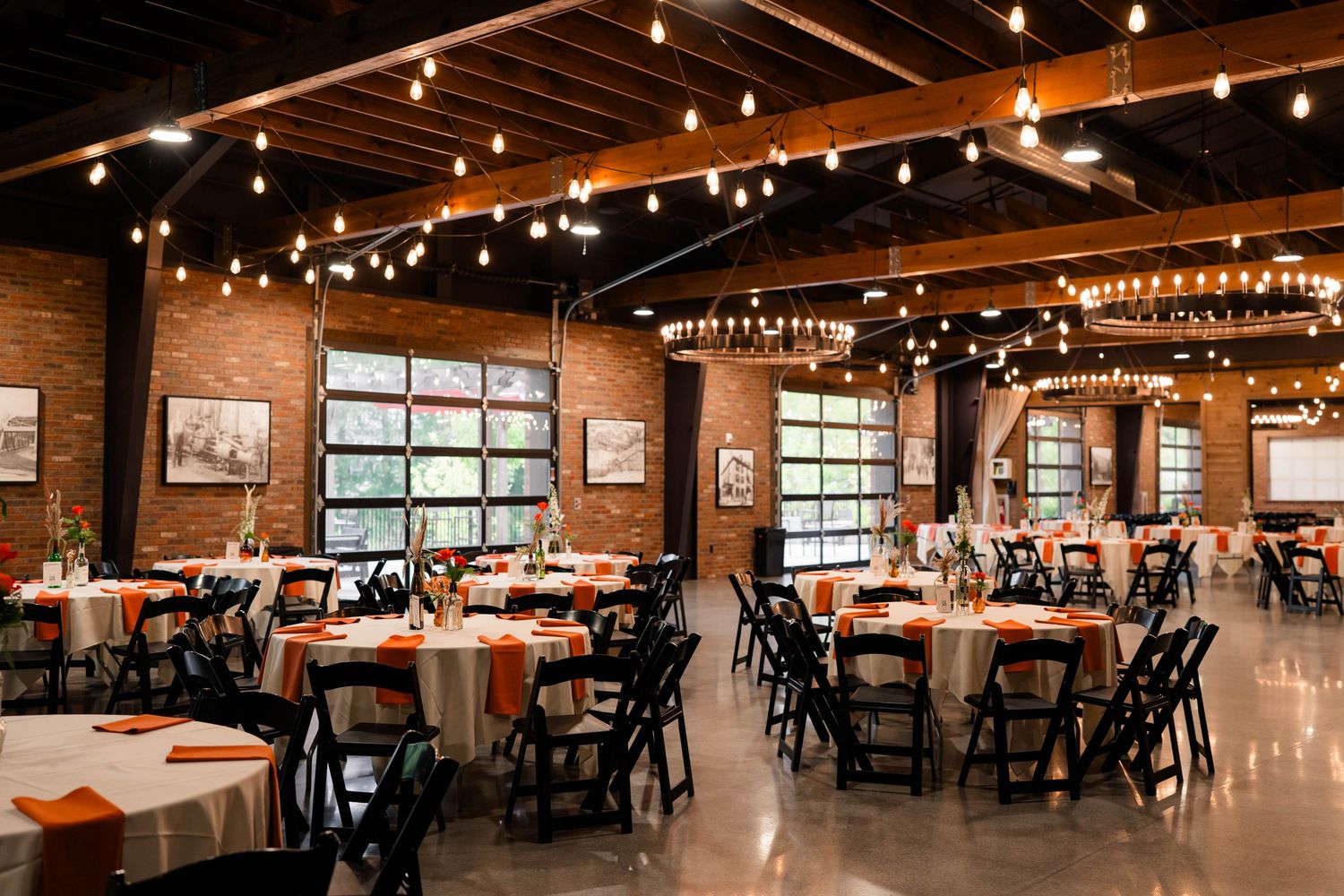 Elegant wedding reception hall with orange table linens, string lights, and exposed brick walls.