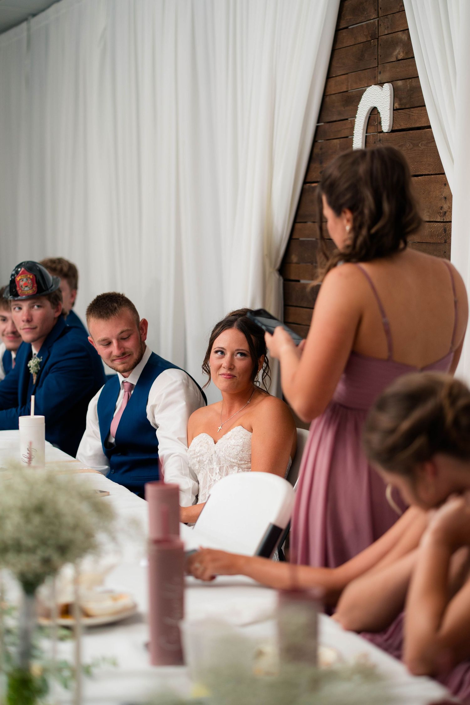 Bride listens attentively as a bridesmaid in a mauve dress reads a wedding speech at the reception.