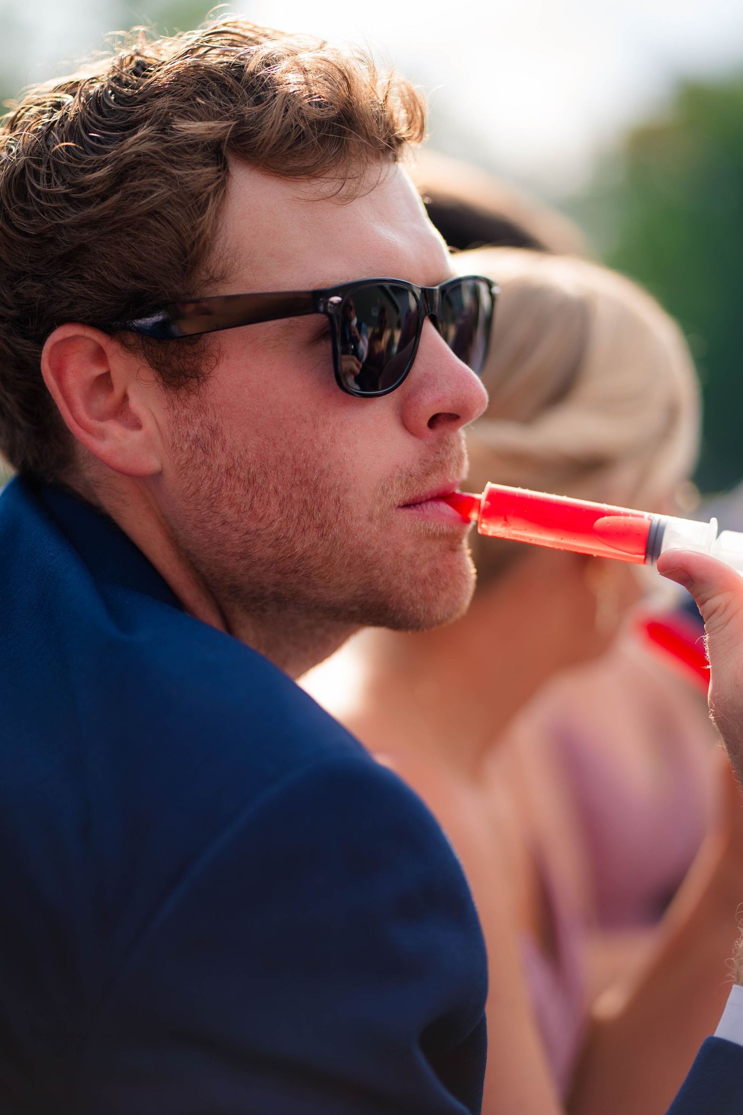 Man in navy suit wearing sunglasses using a vape at a wedding reception.