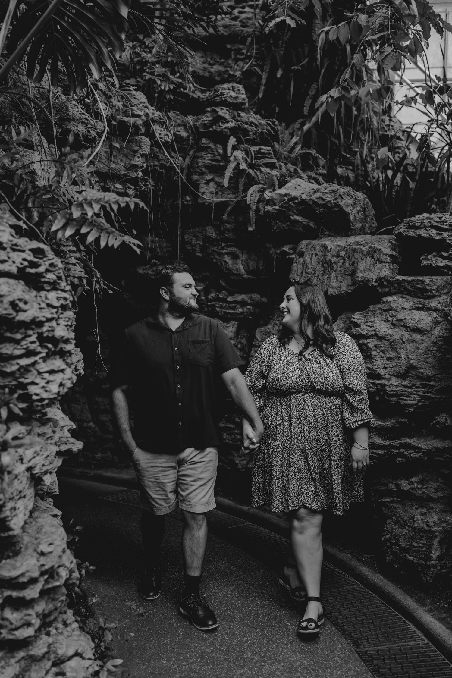 Black and white photo of couple holding hands near rocky walls in a botanical garden.