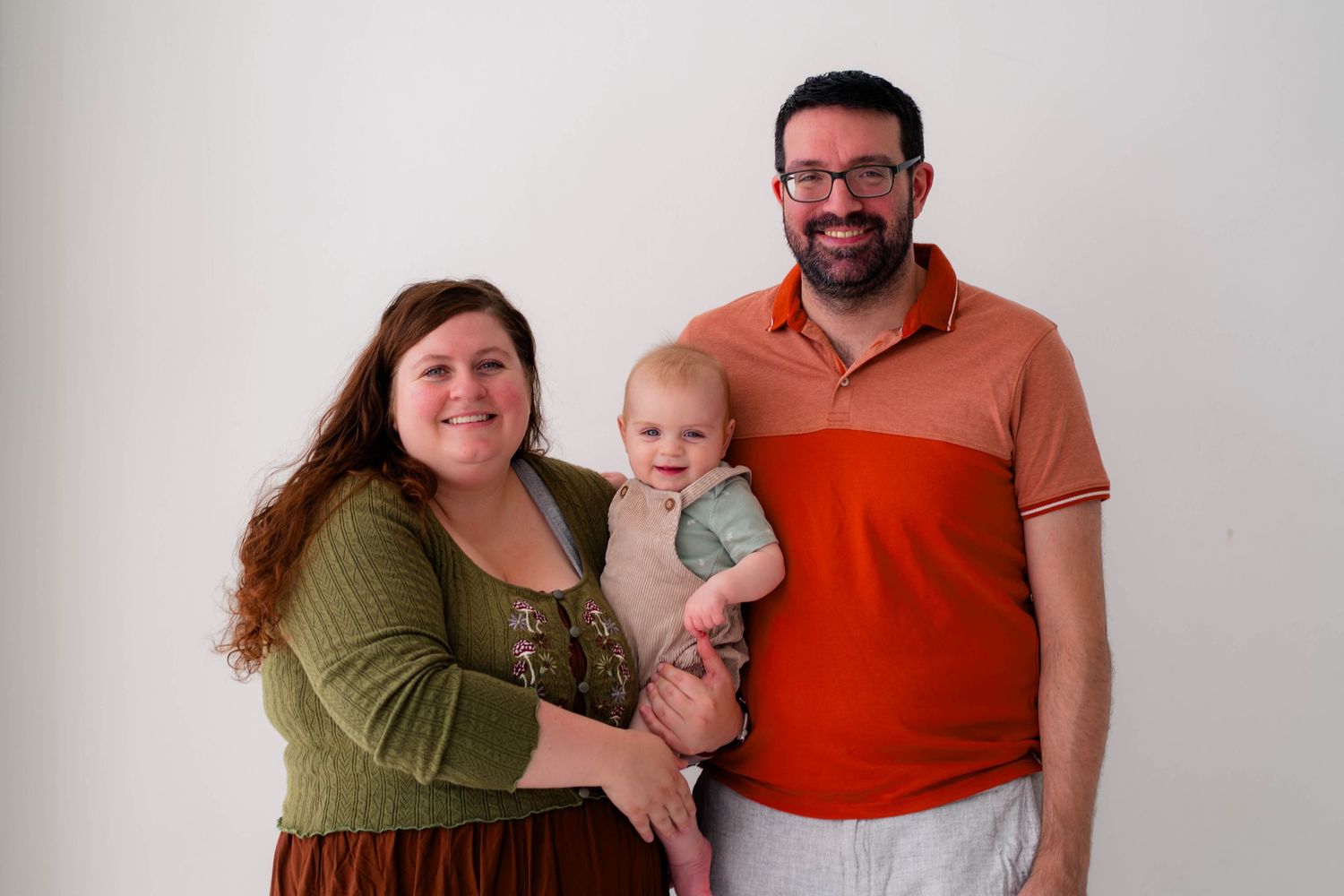 Happy family portrait with mother, father, and baby posed against a white background.
