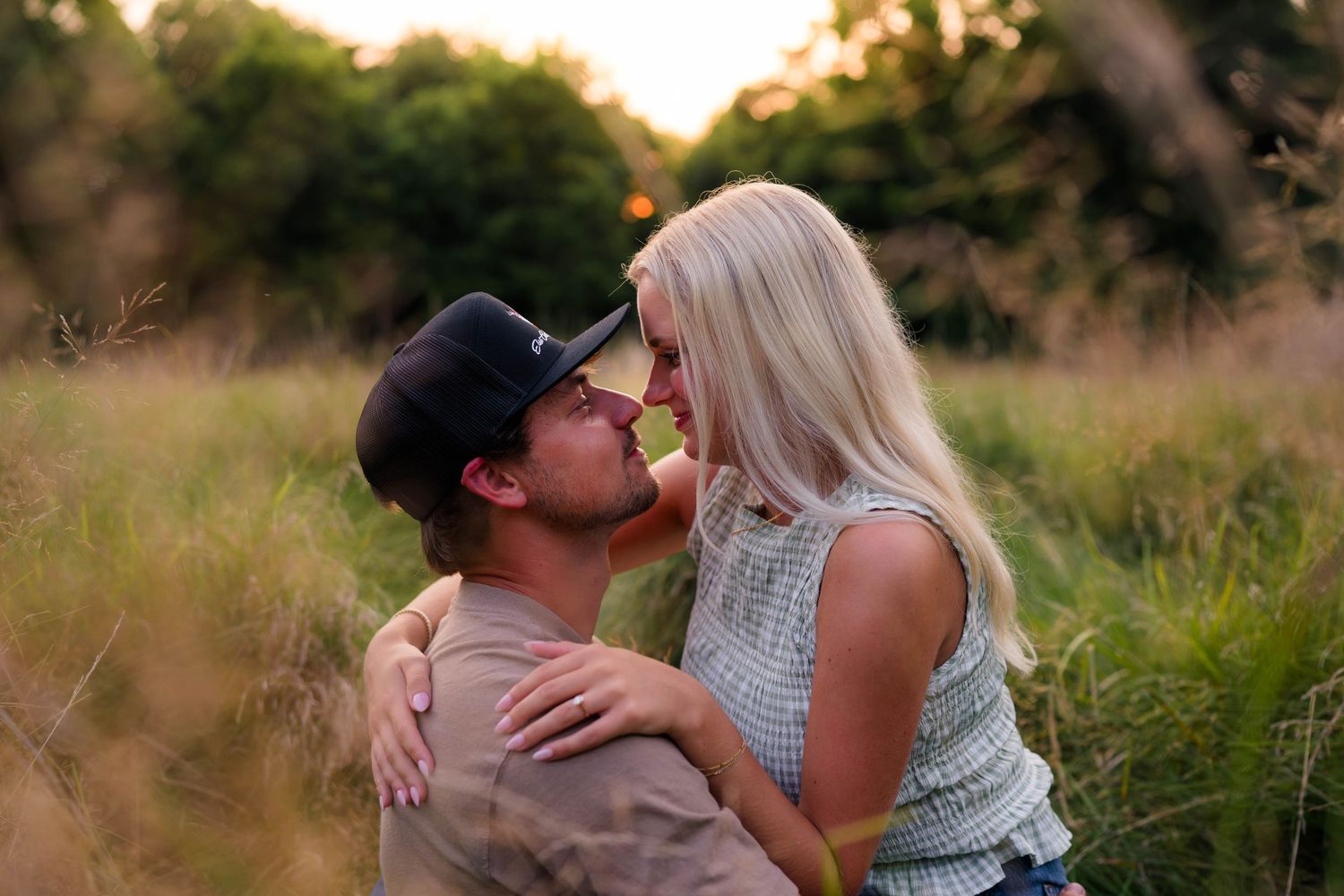Couple sharing a romantic moment about to kiss in a golden sunlit field at sunset.