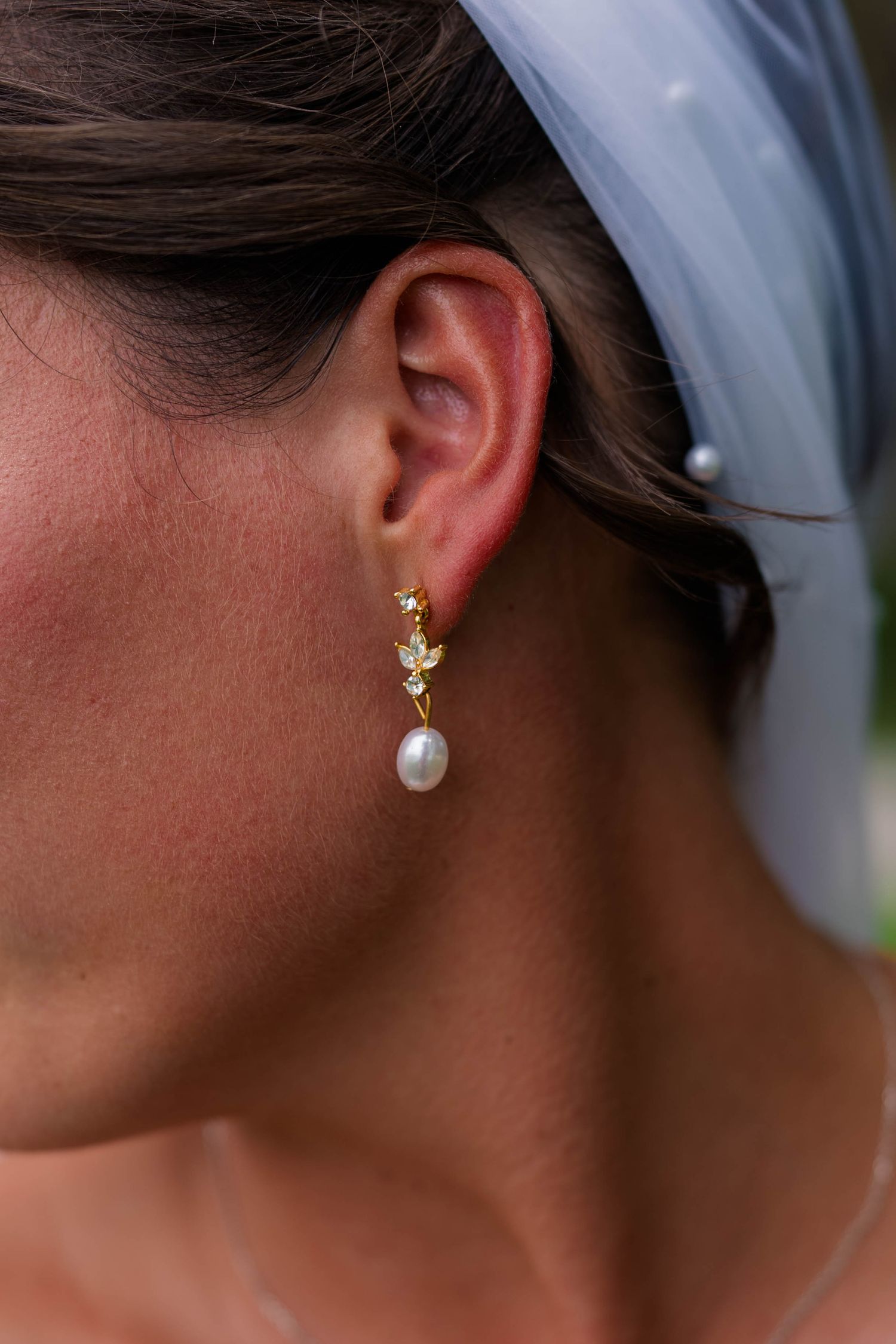 Bride wearing elegant gold drop earring with pearl and crystal details, complemented by a white wedding veil.
