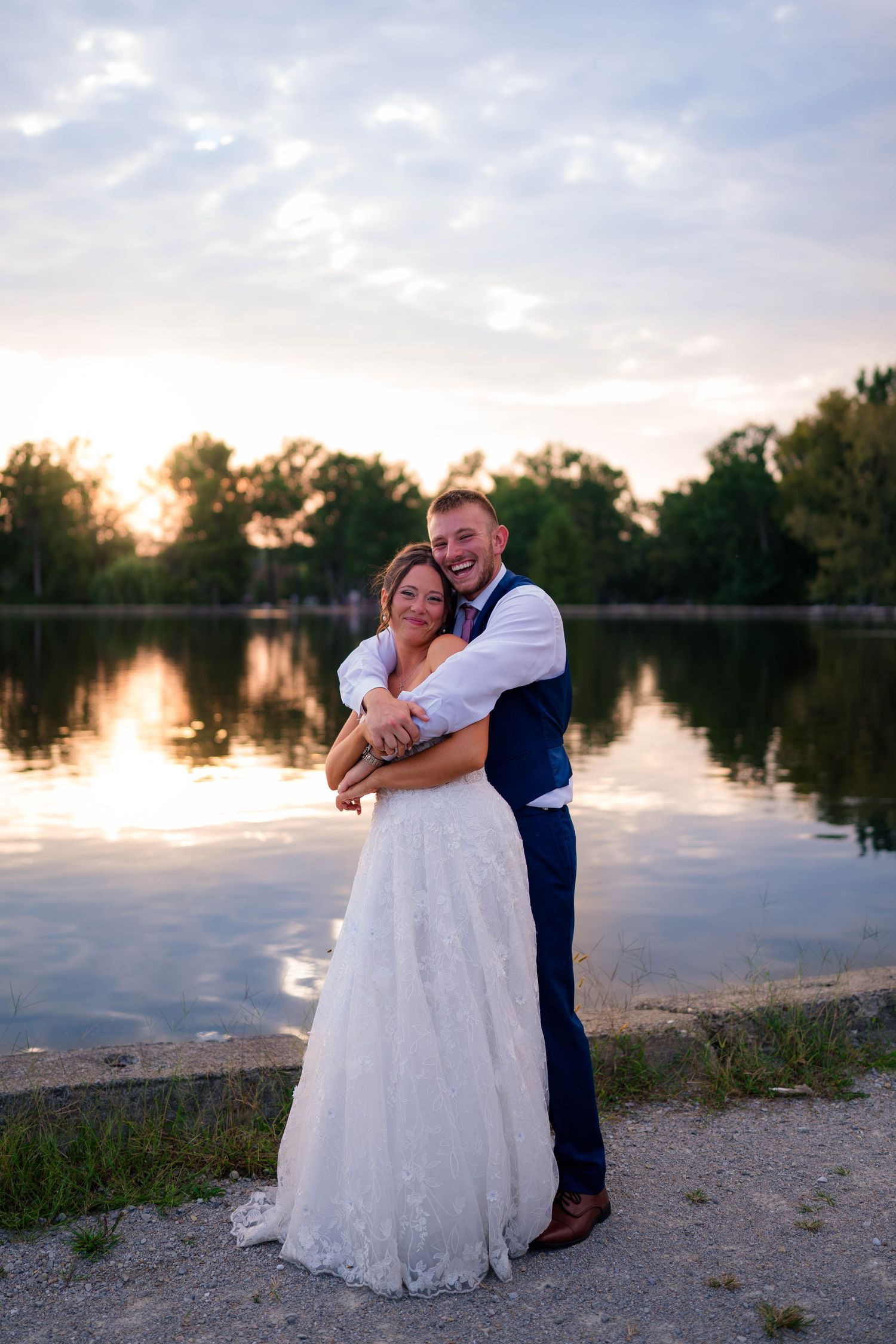 Happy couple embraces and smiles together by a serene lake during golden hour.