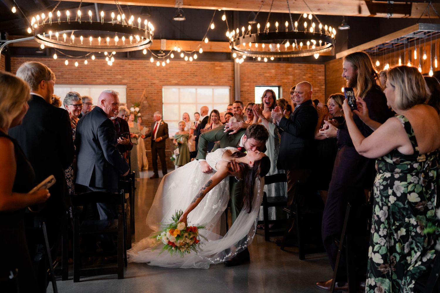 Bride and groom share dramatic dip kiss during wedding reception exit amid cheering guests.