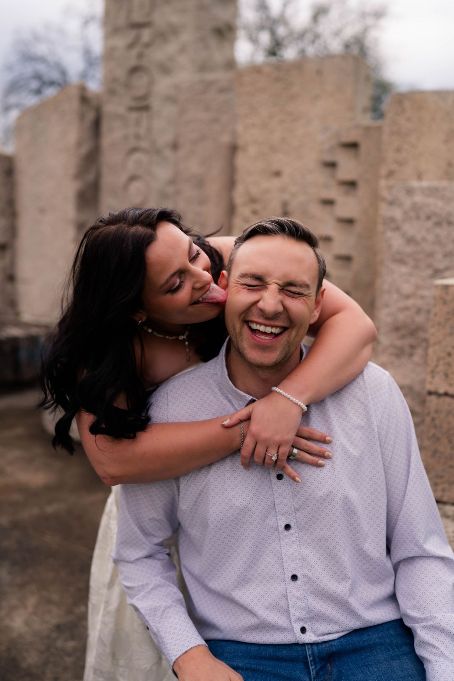 Laughing couple embracing outdoors near stone ruins during engagement photo session.