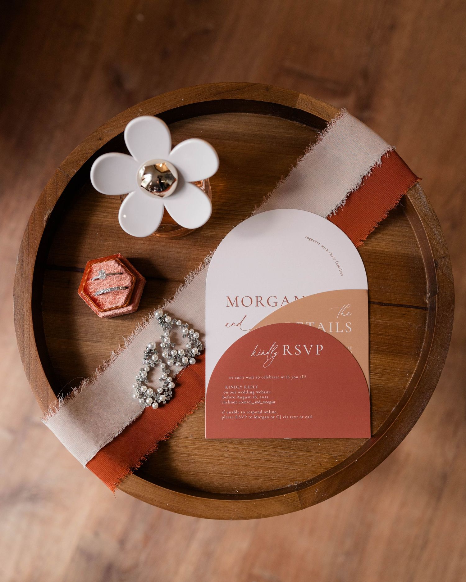 Elegant wedding invitation suite with terracotta arch design, pearl bracelet, and floral ring dish on wooden tray.