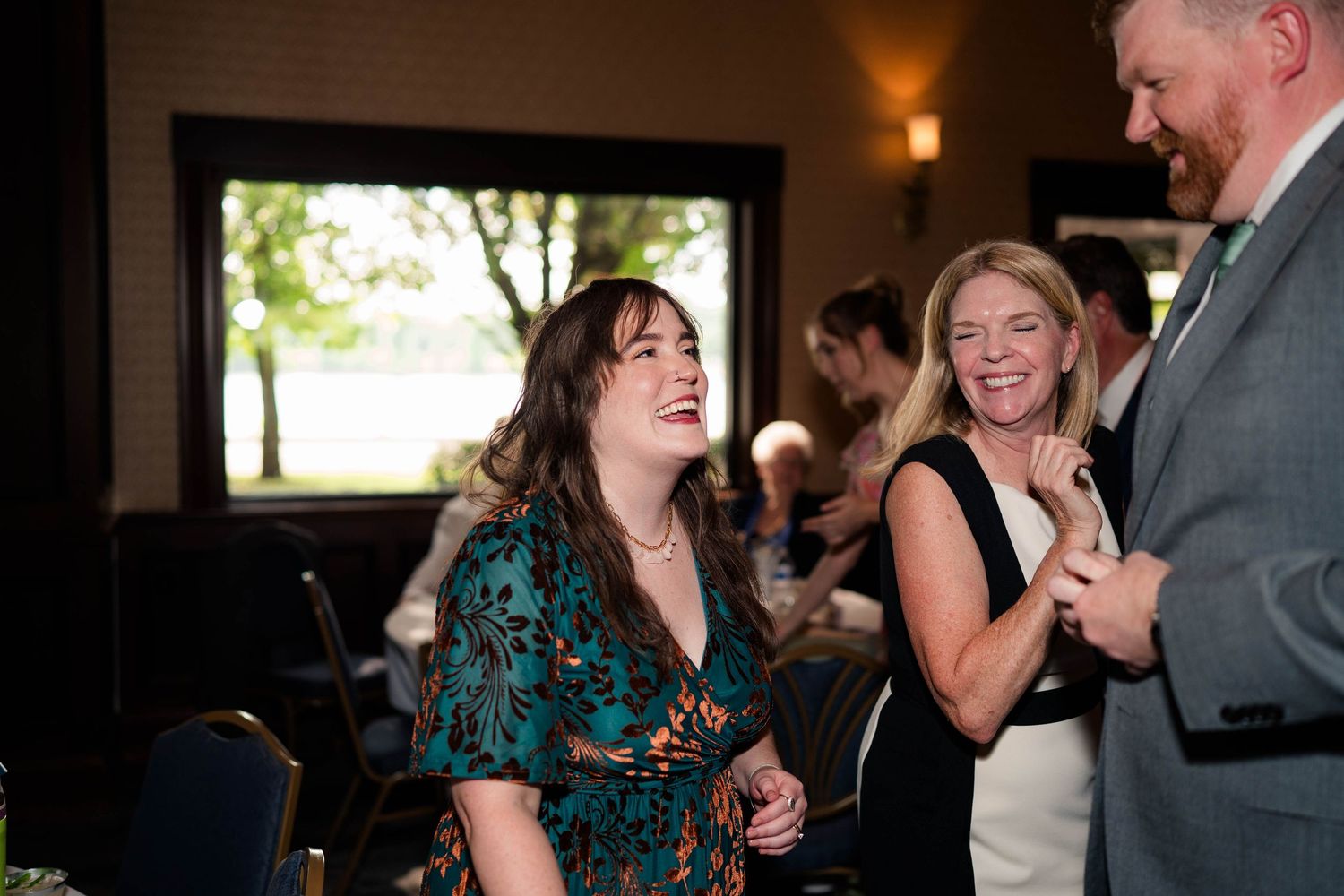 Two women laugh together joyfully at an indoor wedding reception dinner celebration.