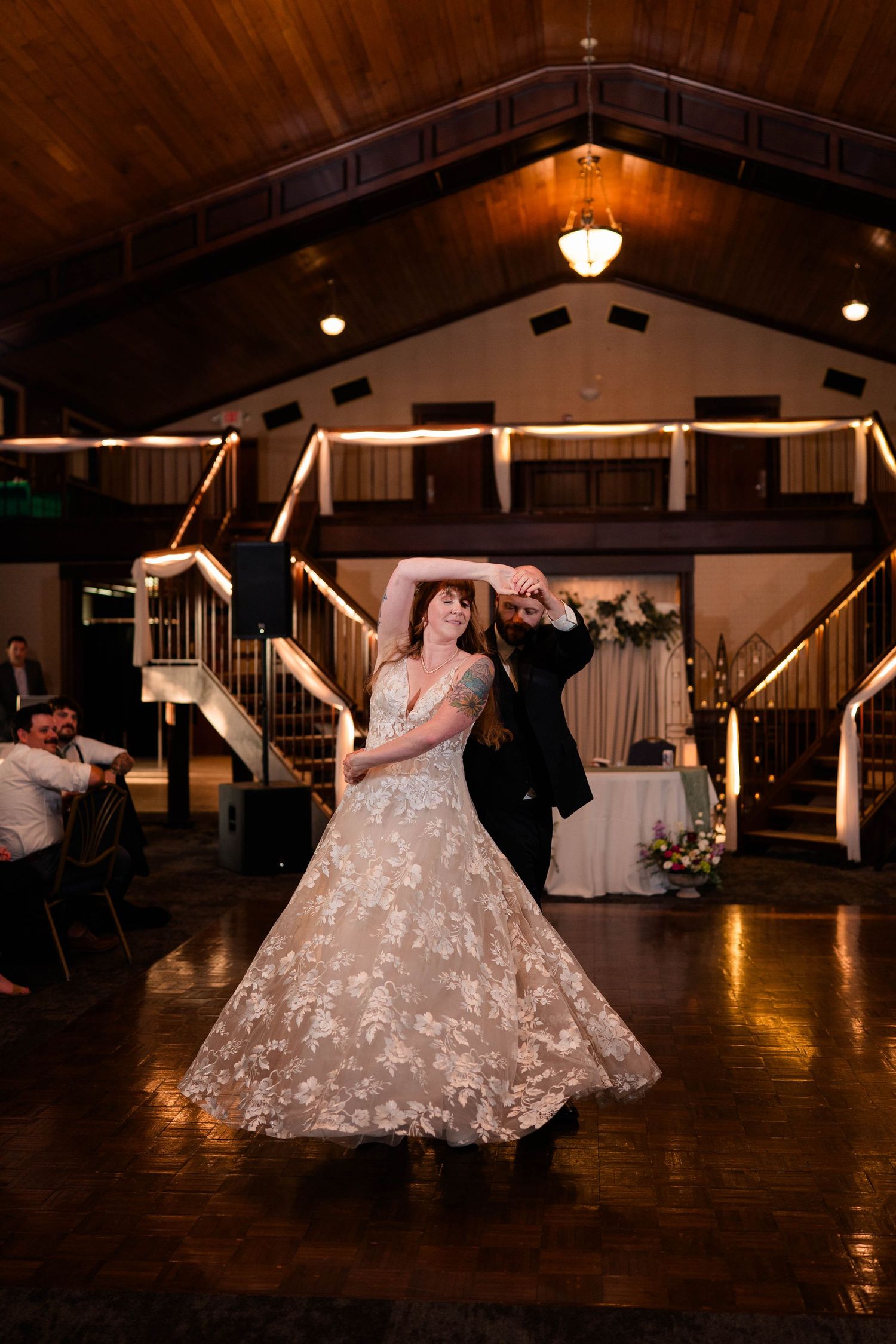 Bride in floral gown twirls with groom during first dance at elegant wedding reception venue.