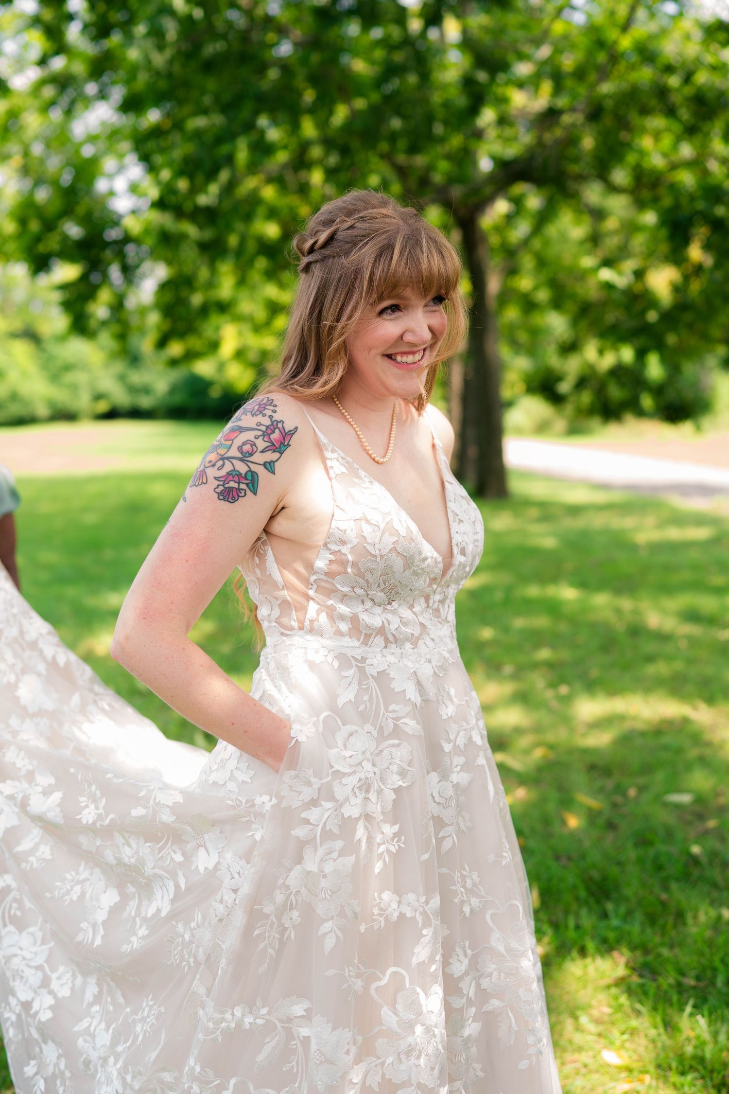 Radiant tattooed bride twirling lace wedding gown in sunny outdoor garden setting.