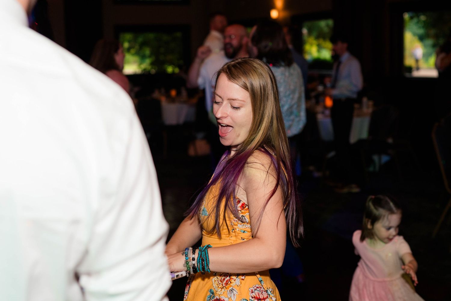 Woman in yellow floral dress dances joyfully at lively wedding reception celebration.