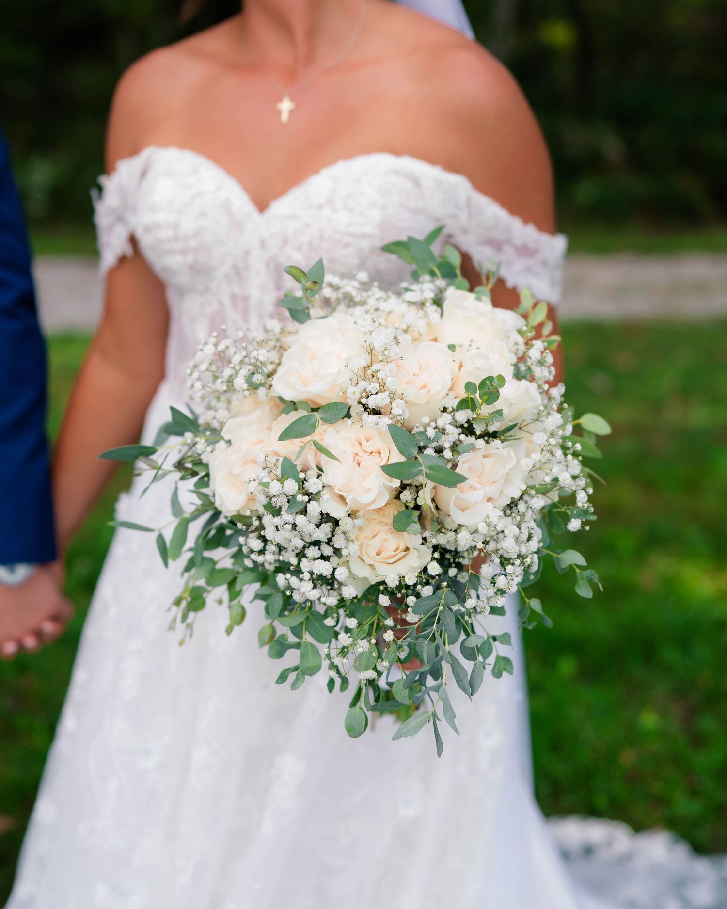 Bride holds a lush white rose and eucalyptus wedding bouquet, wearing an off-shoulder lace gown.