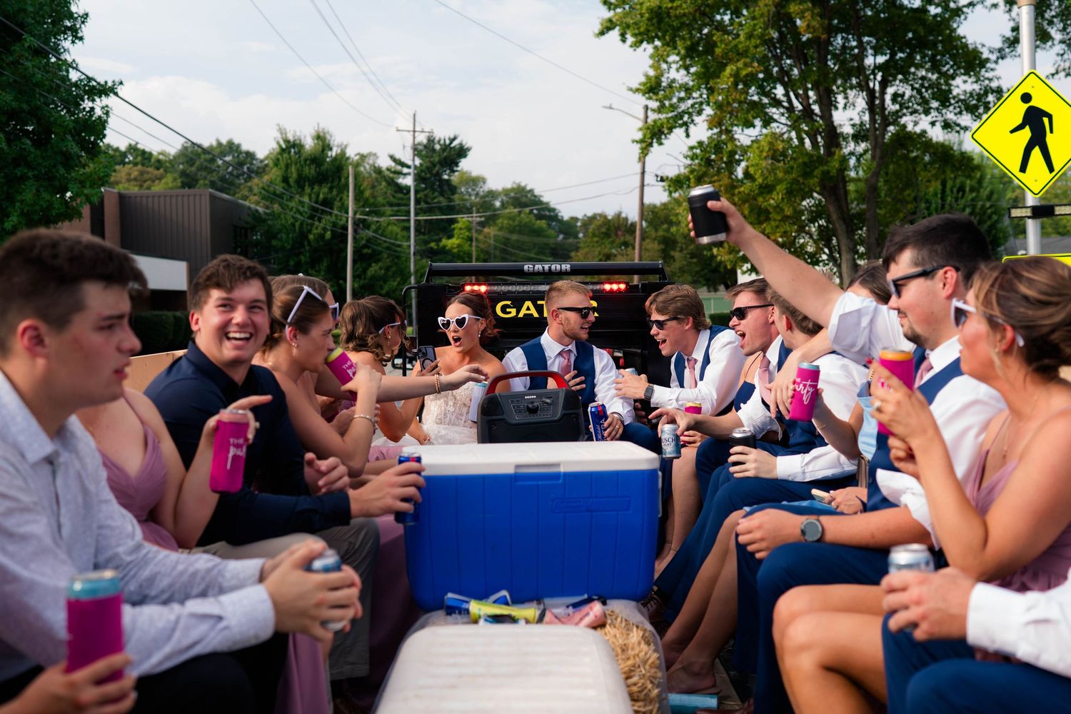 Wedding party guests celebrate on decorated flatbed truck during outdoor reception parade.