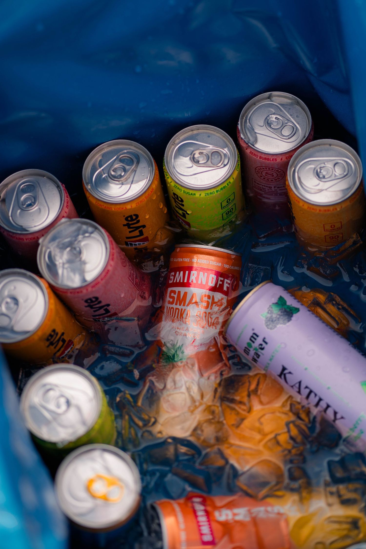 Assorted colorful canned beverages chilling on ice in a blue cooler at a wedding reception.