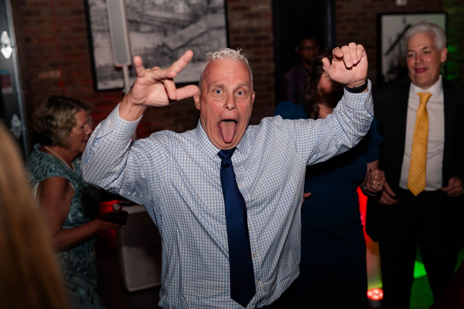 Energetic wedding guest making rock sign with tongue out while celebrating on the dance floor.