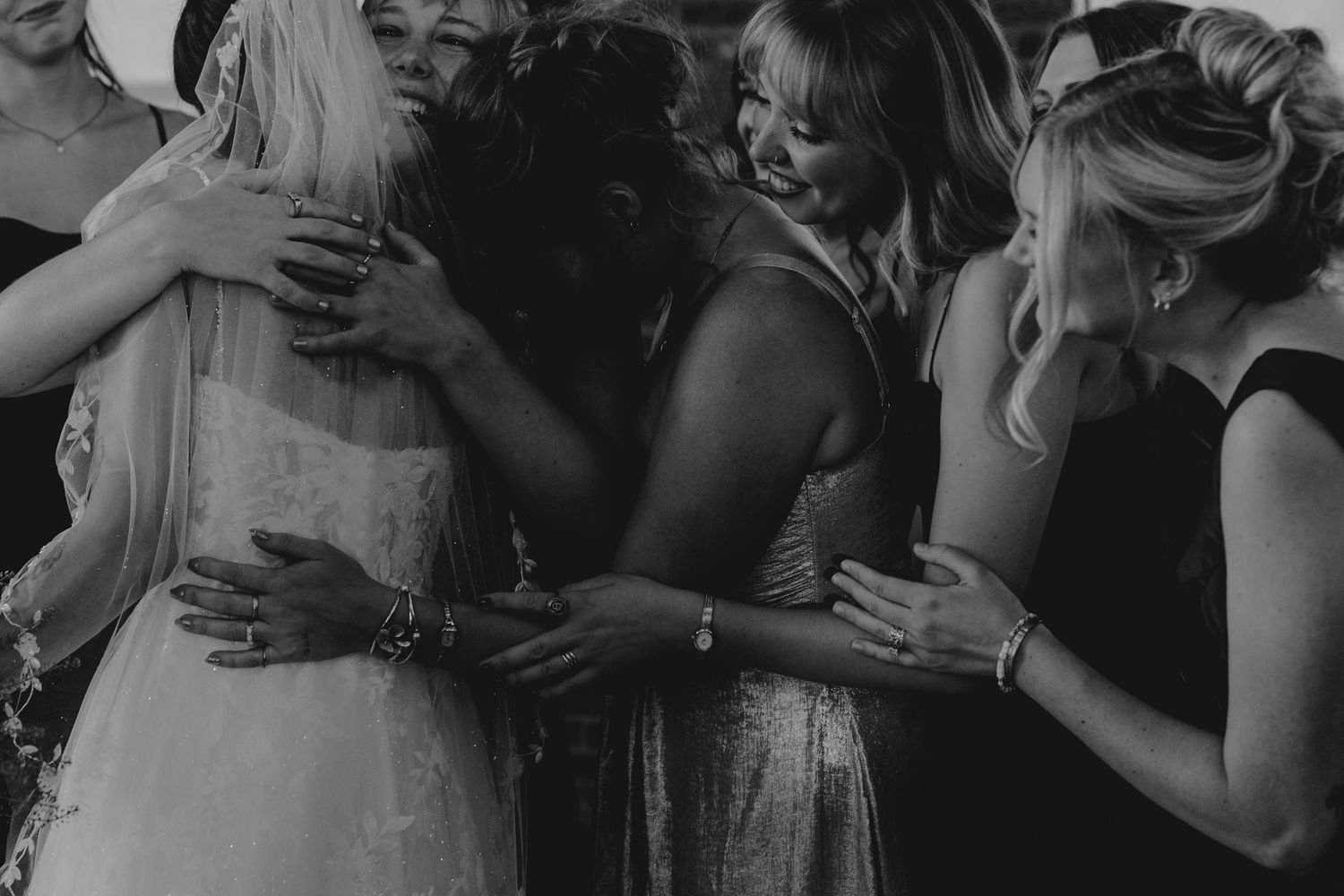 Emotional black and white photo of bride and bridesmaids sharing a group hug during wedding day preparations.