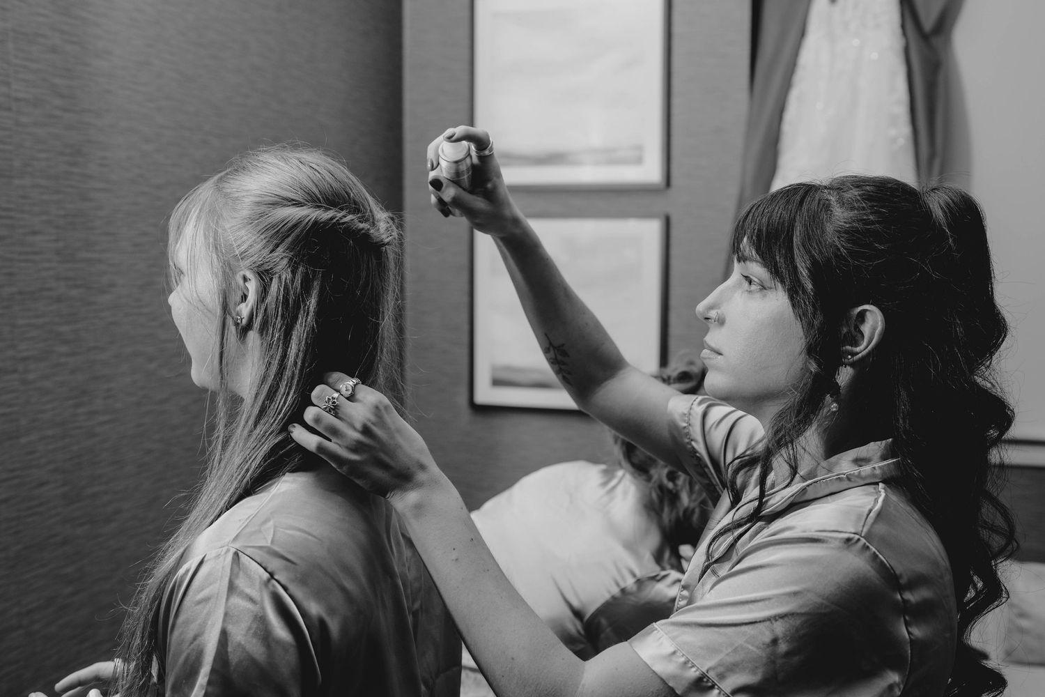 A woman styles another womans long blonde hair in a black and white photo.