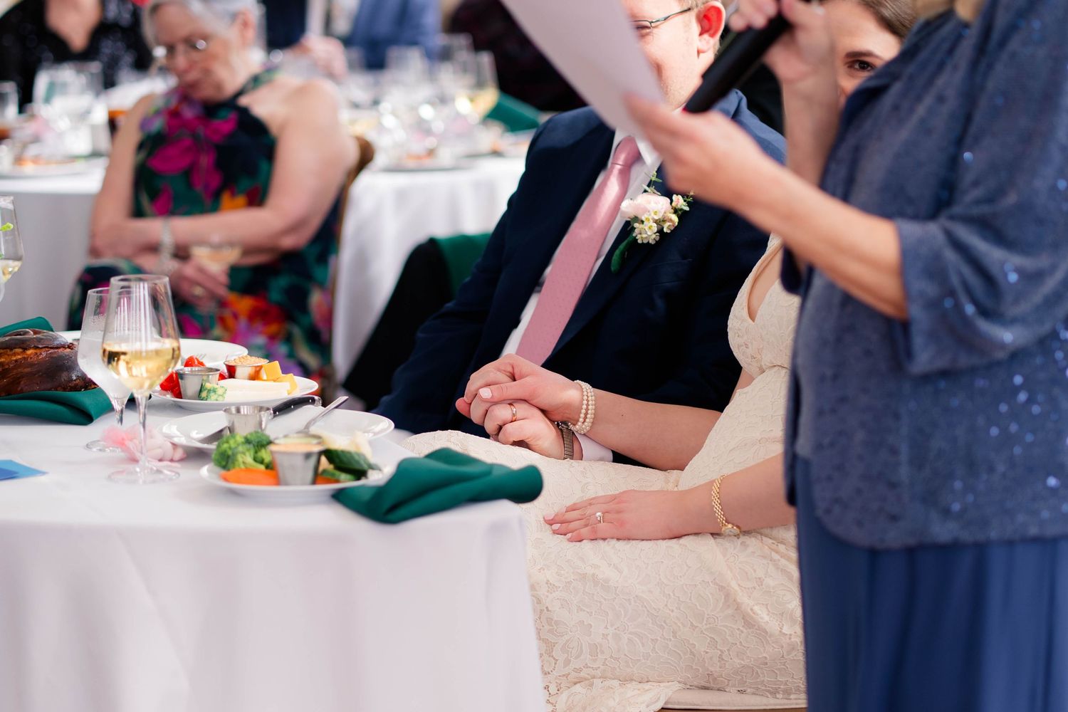 Bride and groom hold hands at sweetheart table during wedding reception toast.