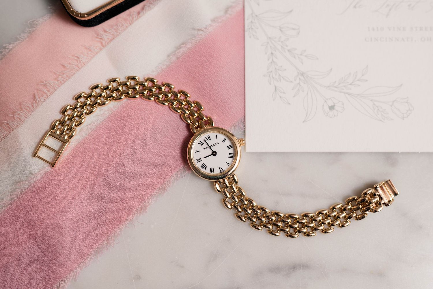 Vintage gold chain-link bracelet watch displayed on marble surface beside wedding invitation.