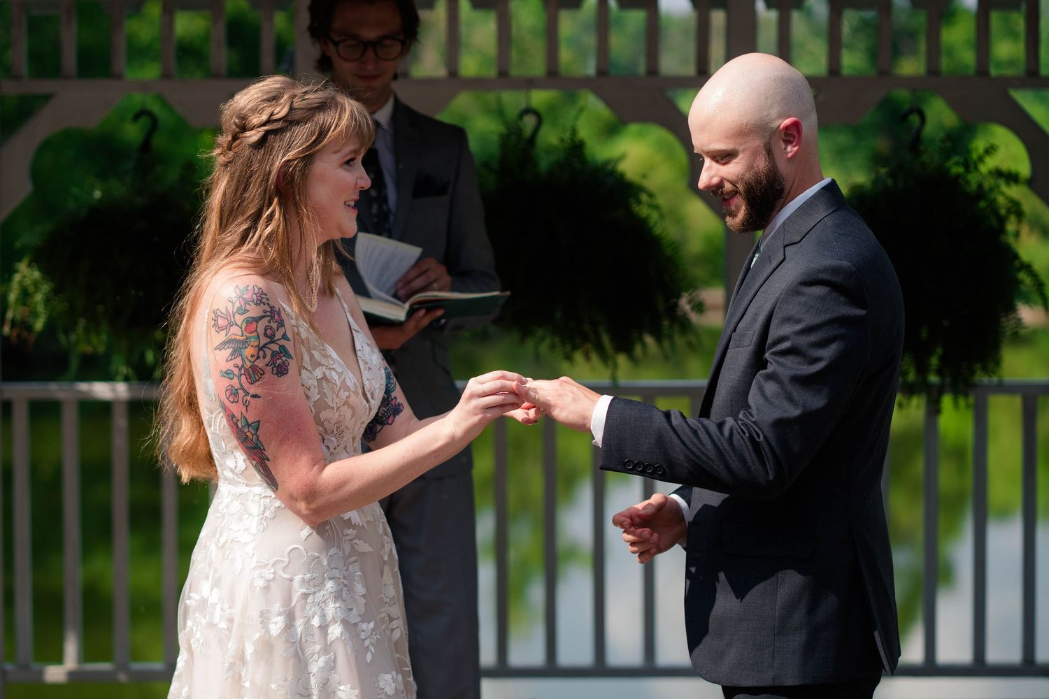 Bride and groom exchange rings and smile joyfully during their outdoor wedding ceremony.