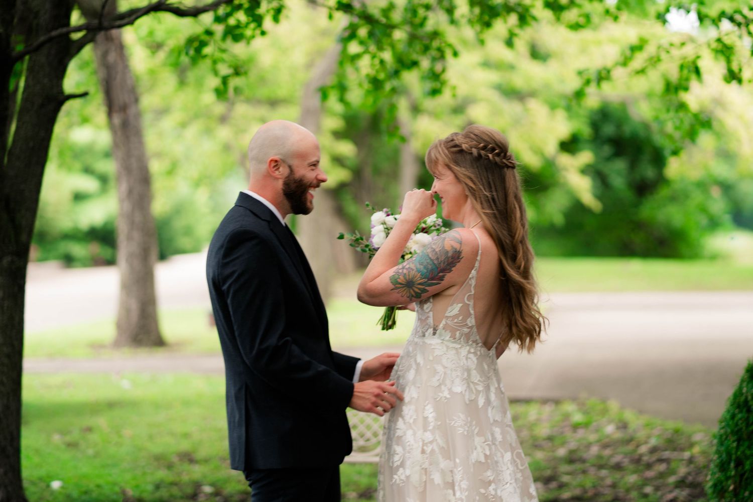 Bride and groom share a tender first look moment under lush green trees during outdoor wedding ceremony.