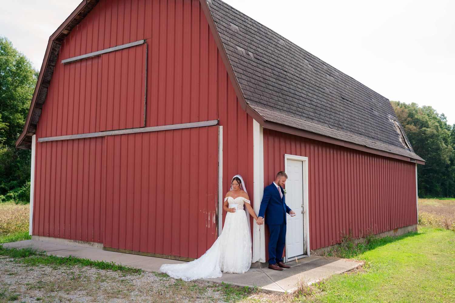Bride and groom holding hands during first look outside a classic red barn on their wedding day.