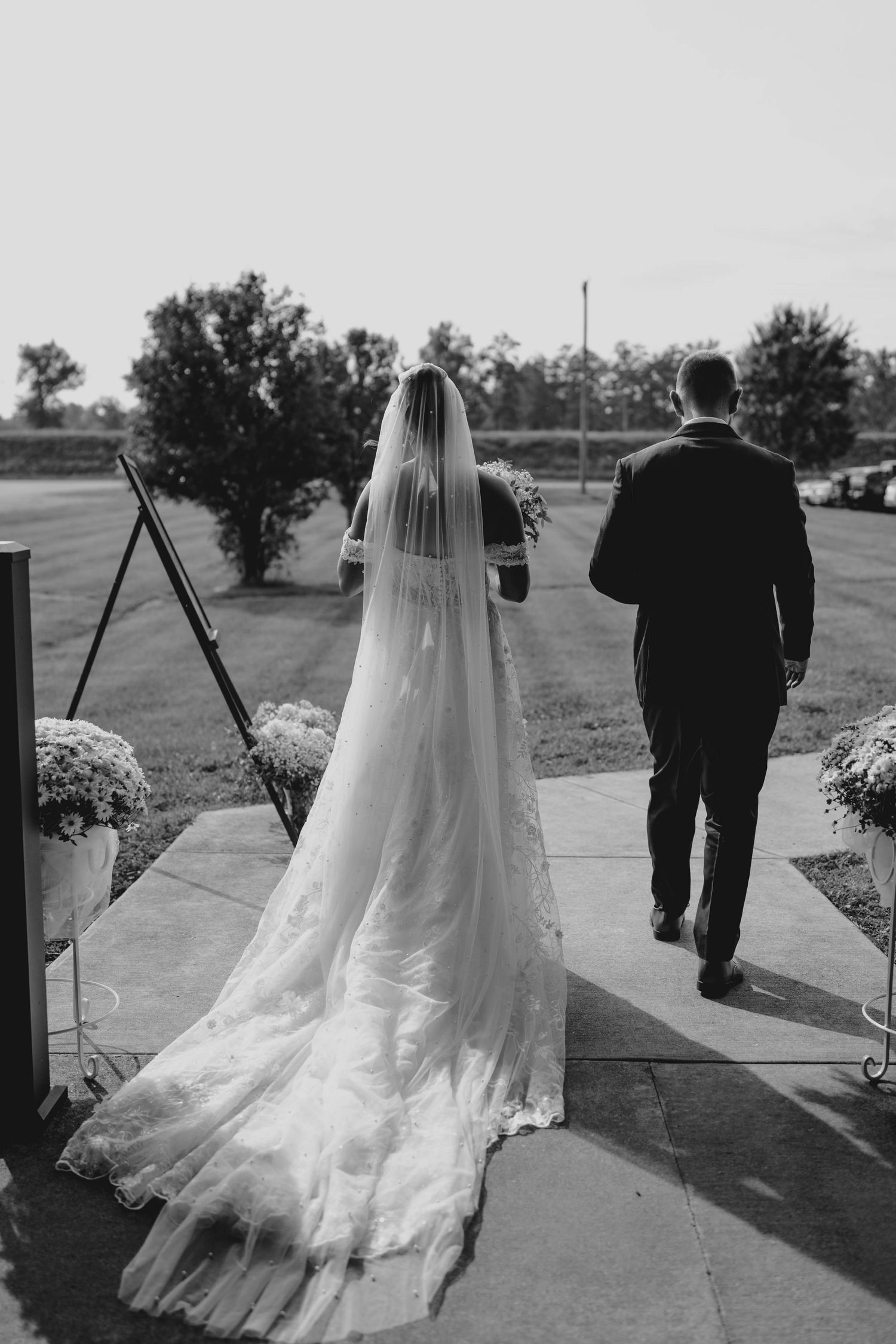 Black and white photo of bride in cathedral veil and groom walking away from ceremony.