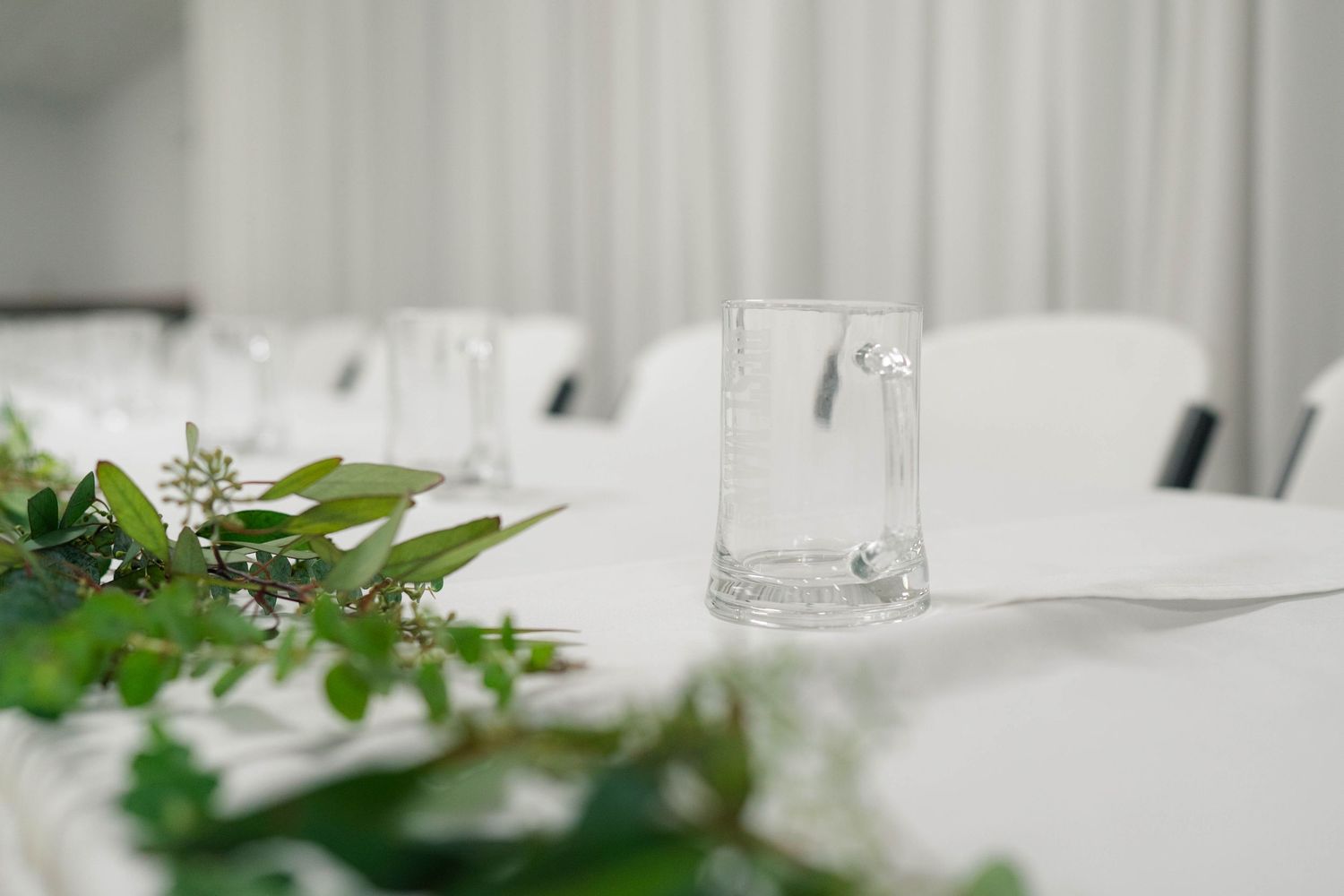 Elegant wedding reception table with clear glassware and fresh green botanical garland centerpiece.