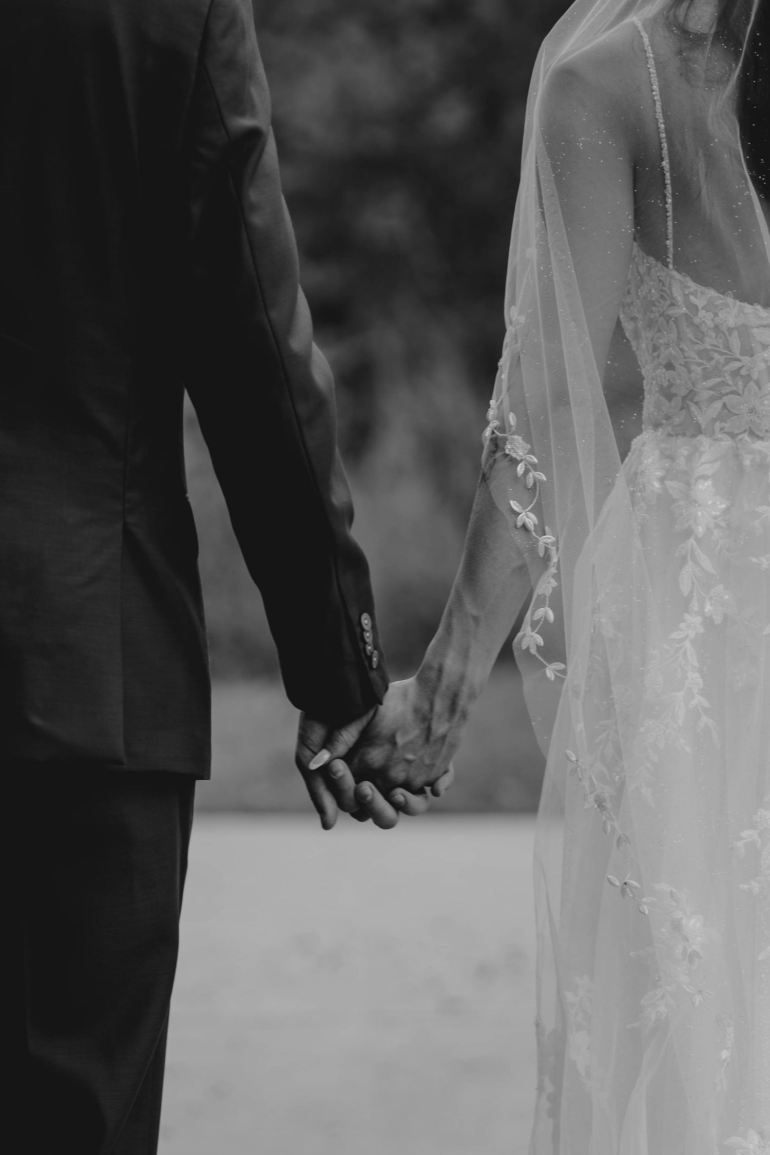 Black and white close-up of newlyweds holding hands outdoors after wedding ceremony.