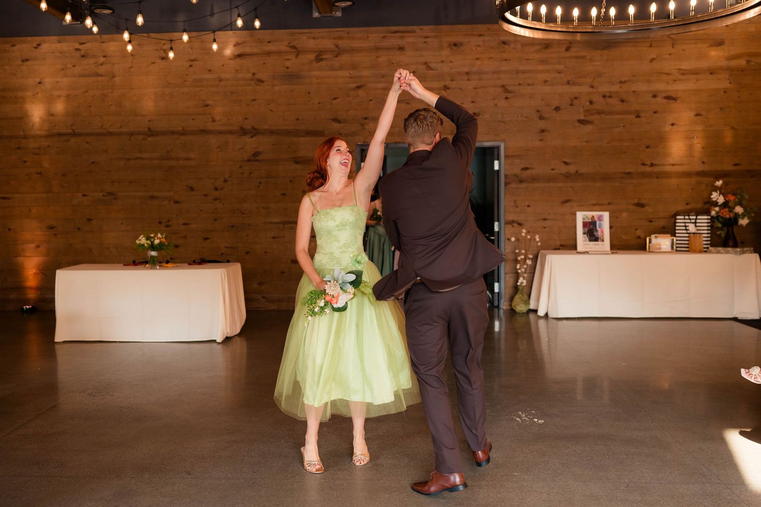 Bride in green dress dancing with groom during first dance at wedding reception.