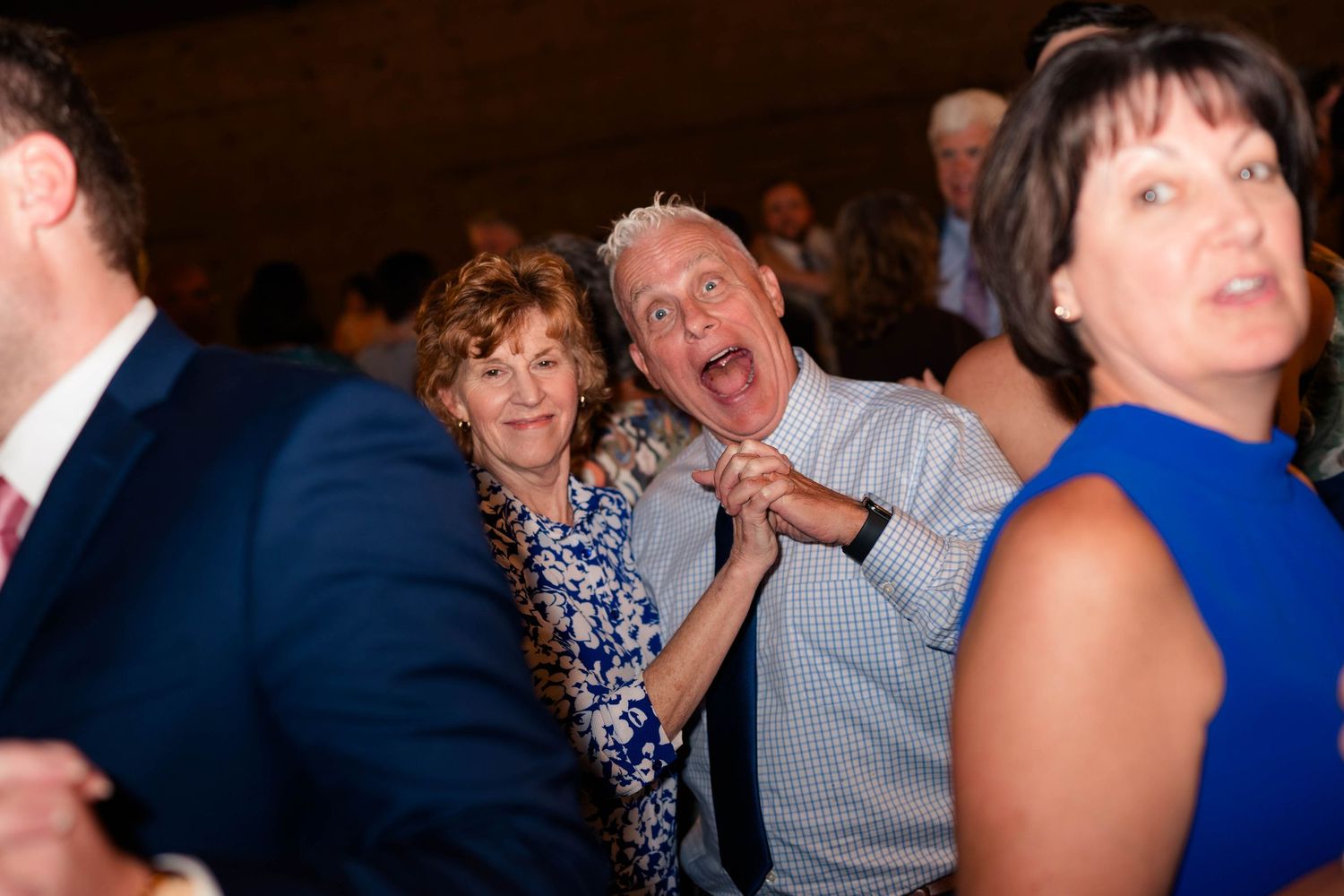 Joyful older couple dancing and laughing at a lively wedding reception.
