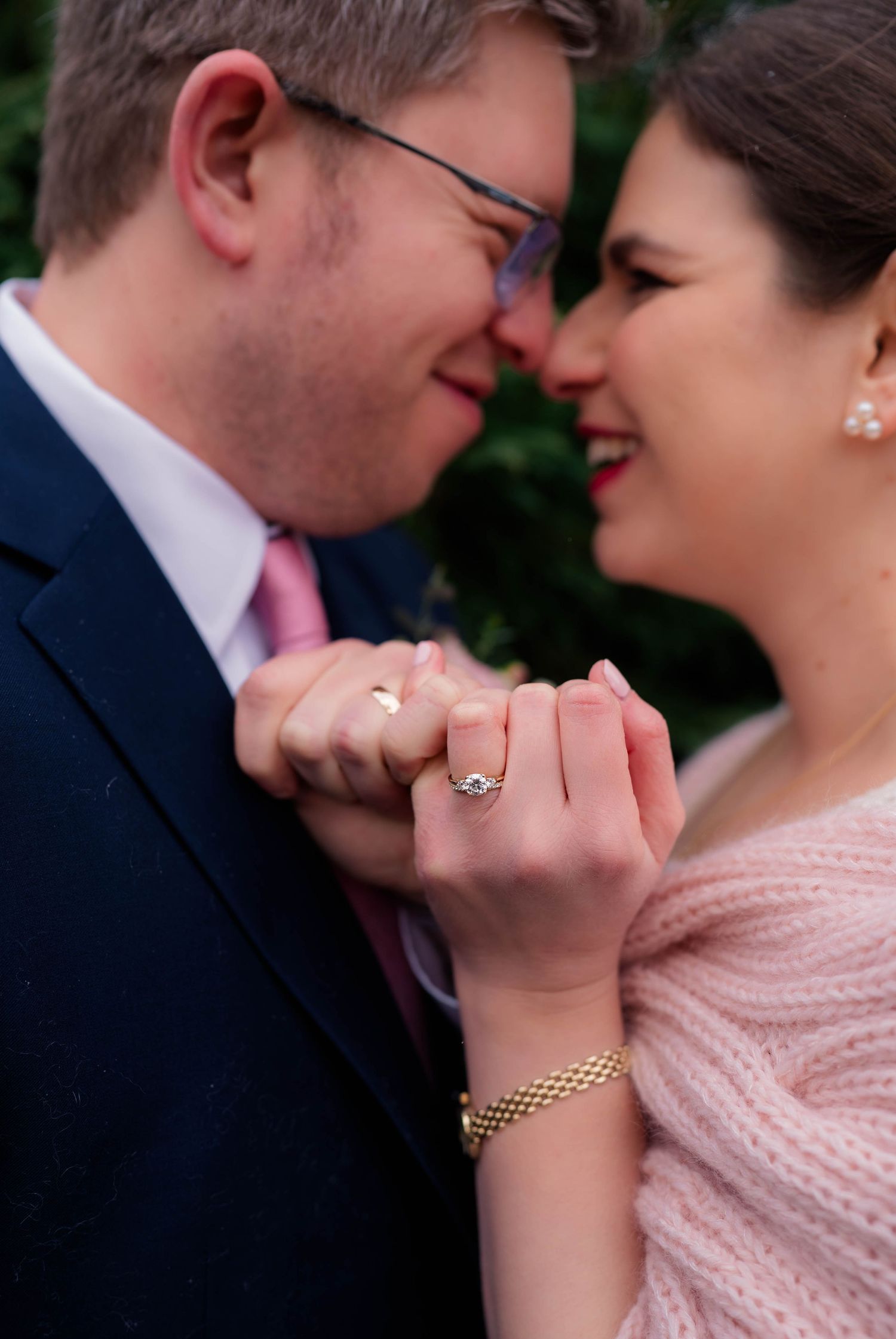 Close-up of bride and groom nearly kissing, showcasing her diamond engagement ring and gold bracelet.